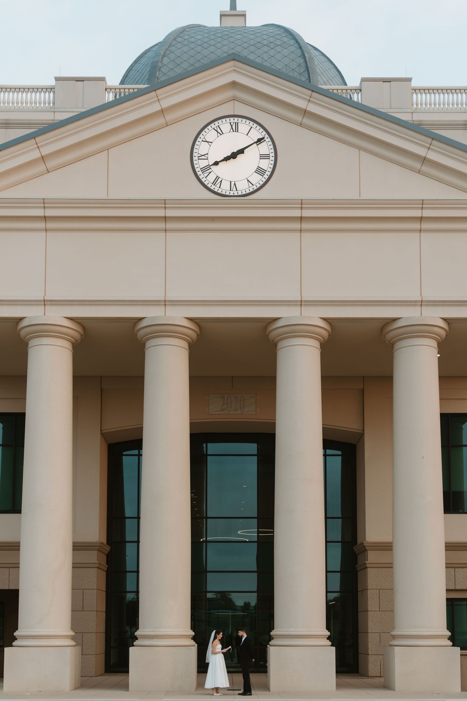 Classical building entrance with white columns, domed roof and large clock, featuring elegant architectural details.