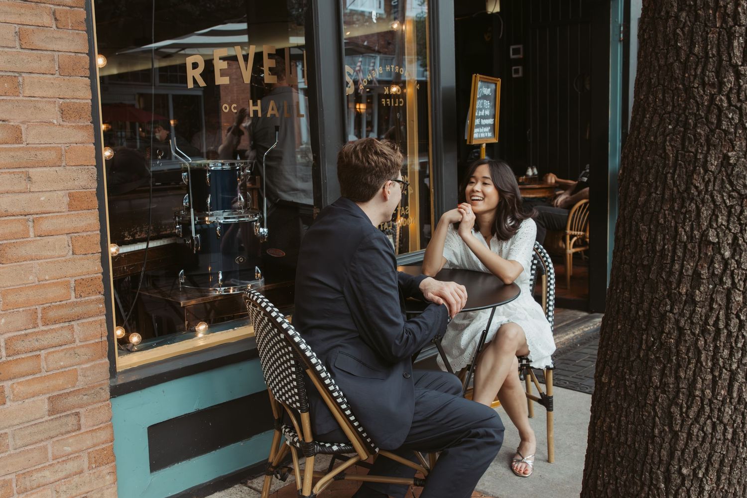 Customers sit at outdoor tables in front of a brick building with large windows and a teal-colored storefront.  Engagement photographer DFW