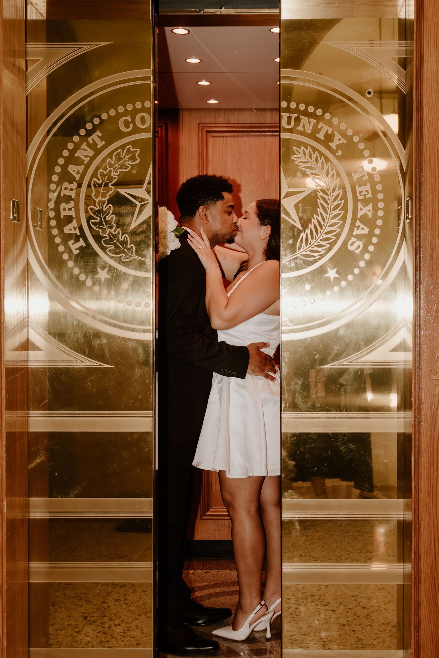 A couple shares an intimate moment in front of decorative glass doors with etched designs. Wedding Photographer DFW