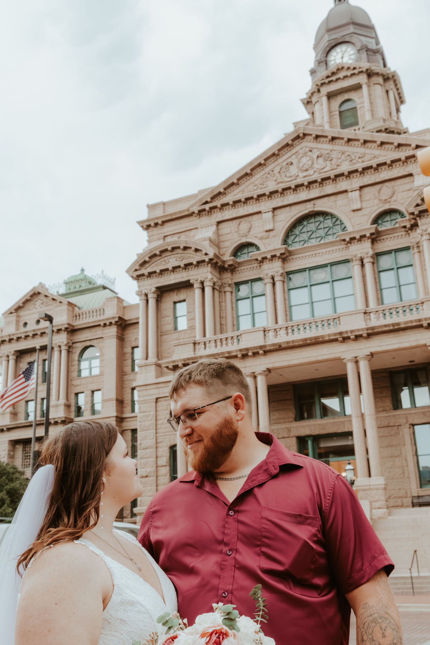 Newlyweds pose in front of a majestic limestone courthouse with classical architecture.