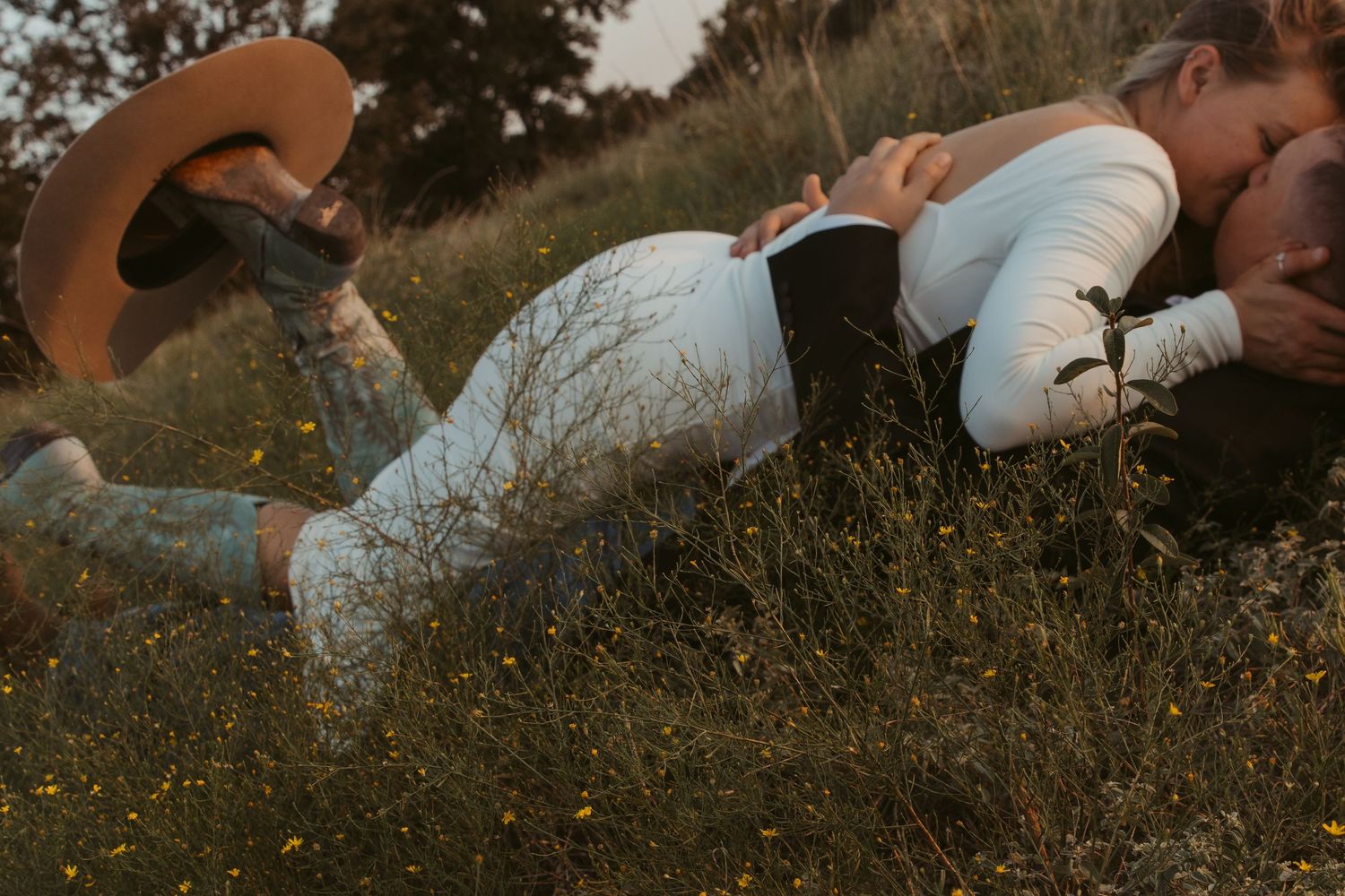 A couple lies together in a grassy meadow during golden hour creating a romantic outdoor scene.