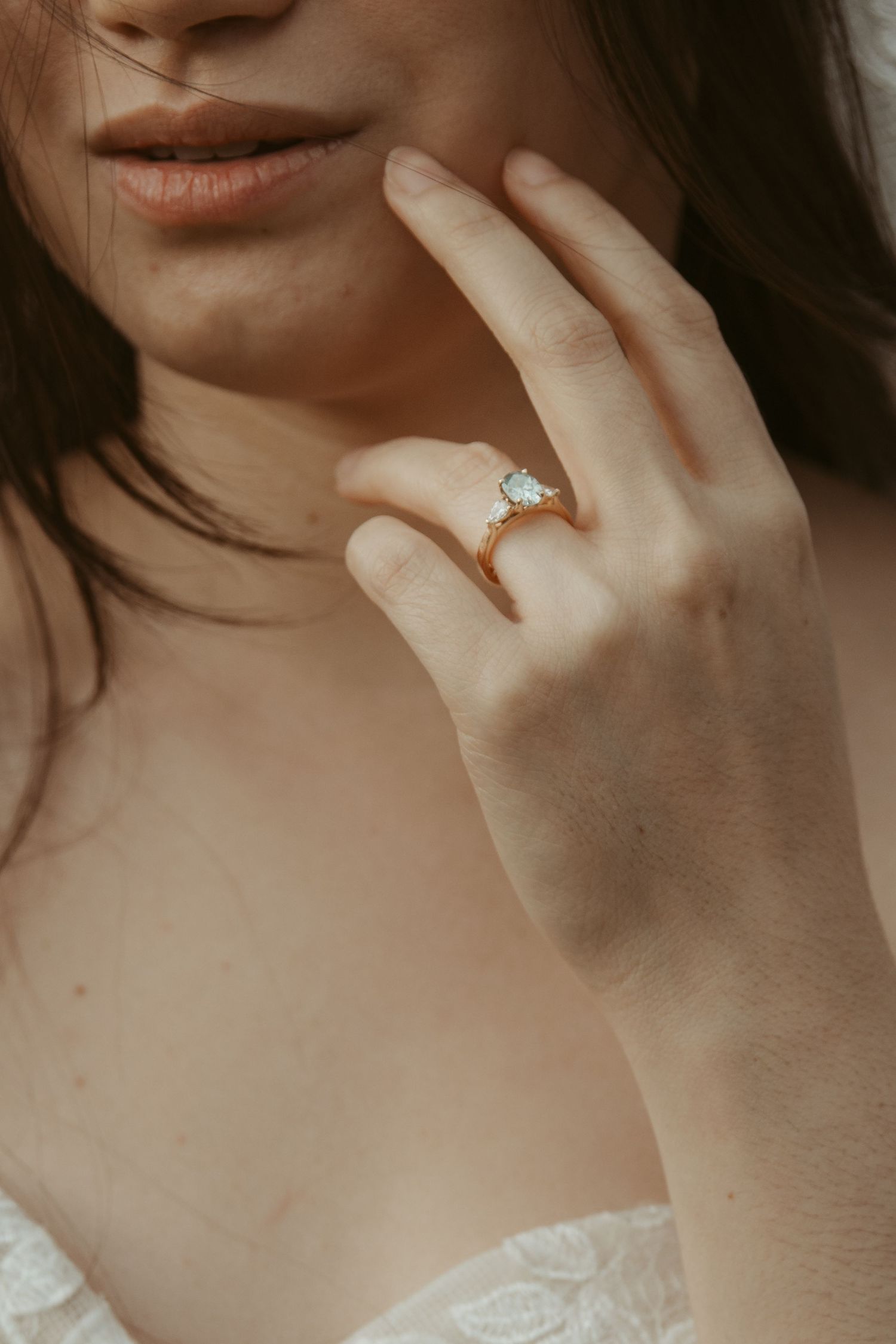 Close-up of a delicate hand wearing an elegant diamond engagement ring against soft white lace fabric.
