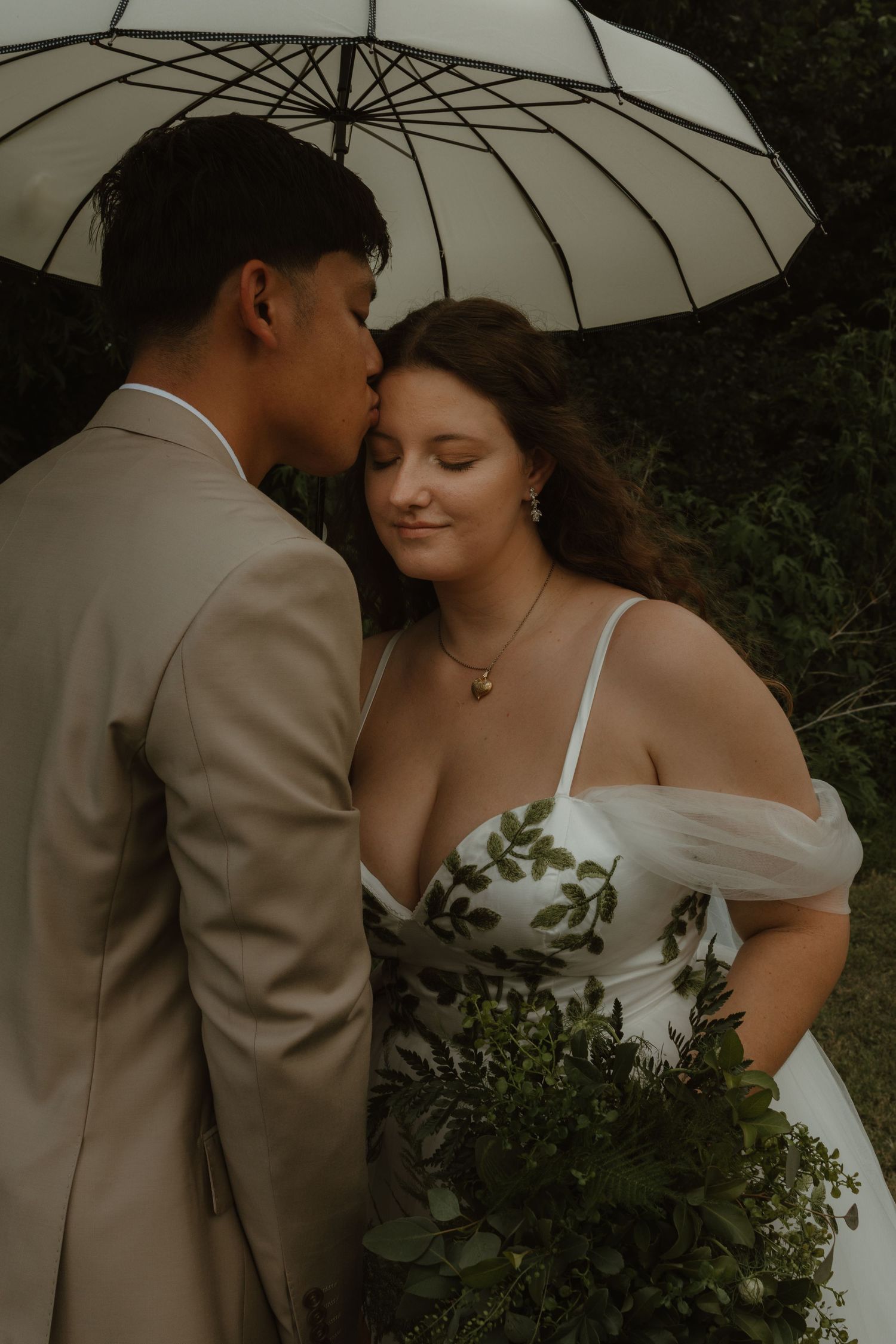 Intimate moment between newlyweds under a white umbrella in romantic lighting.