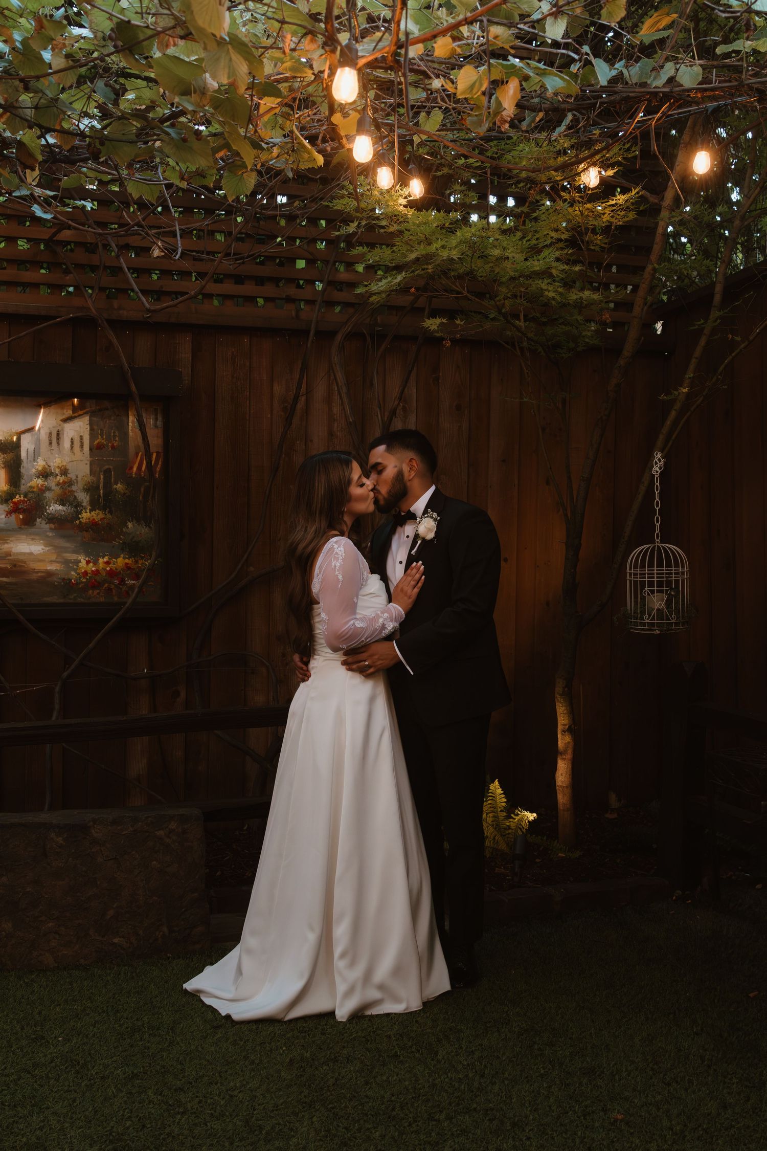 A romantic garden wedding scene with string lights overhead and a couple sharing an intimate moment at dusk.