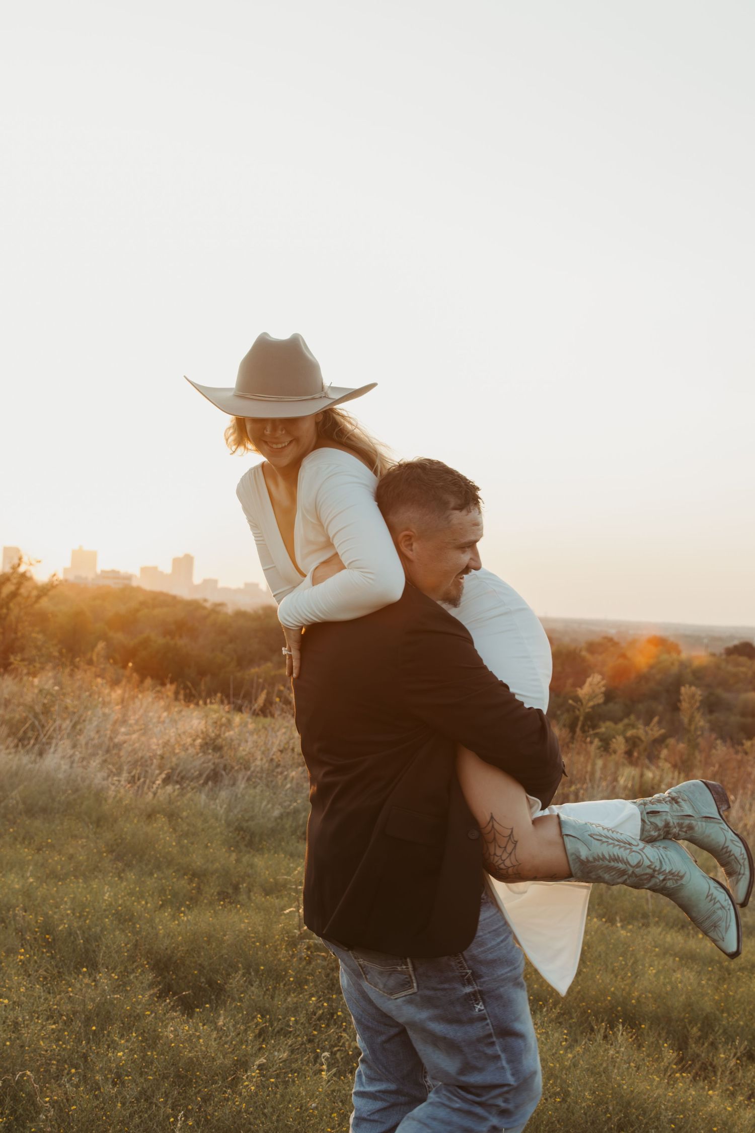 Romantic sunset embrace with cowboy hat against a golden field backdrop during a rustic countryside photoshoot.