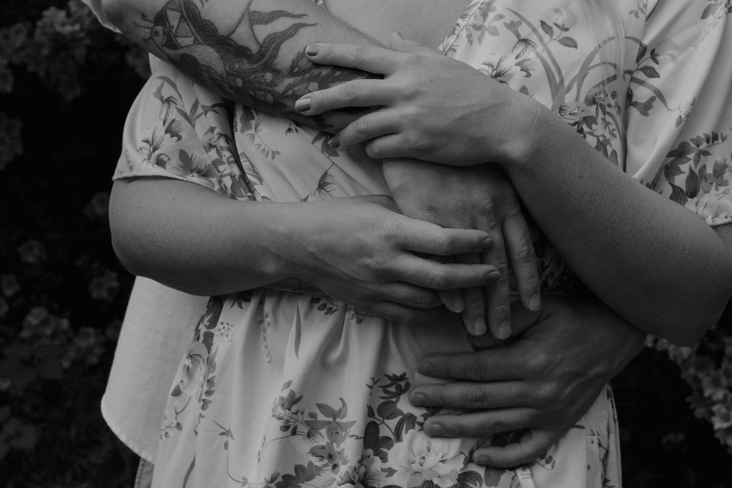 Black and white close up of hands grasping and embracing a floral dress fabric.