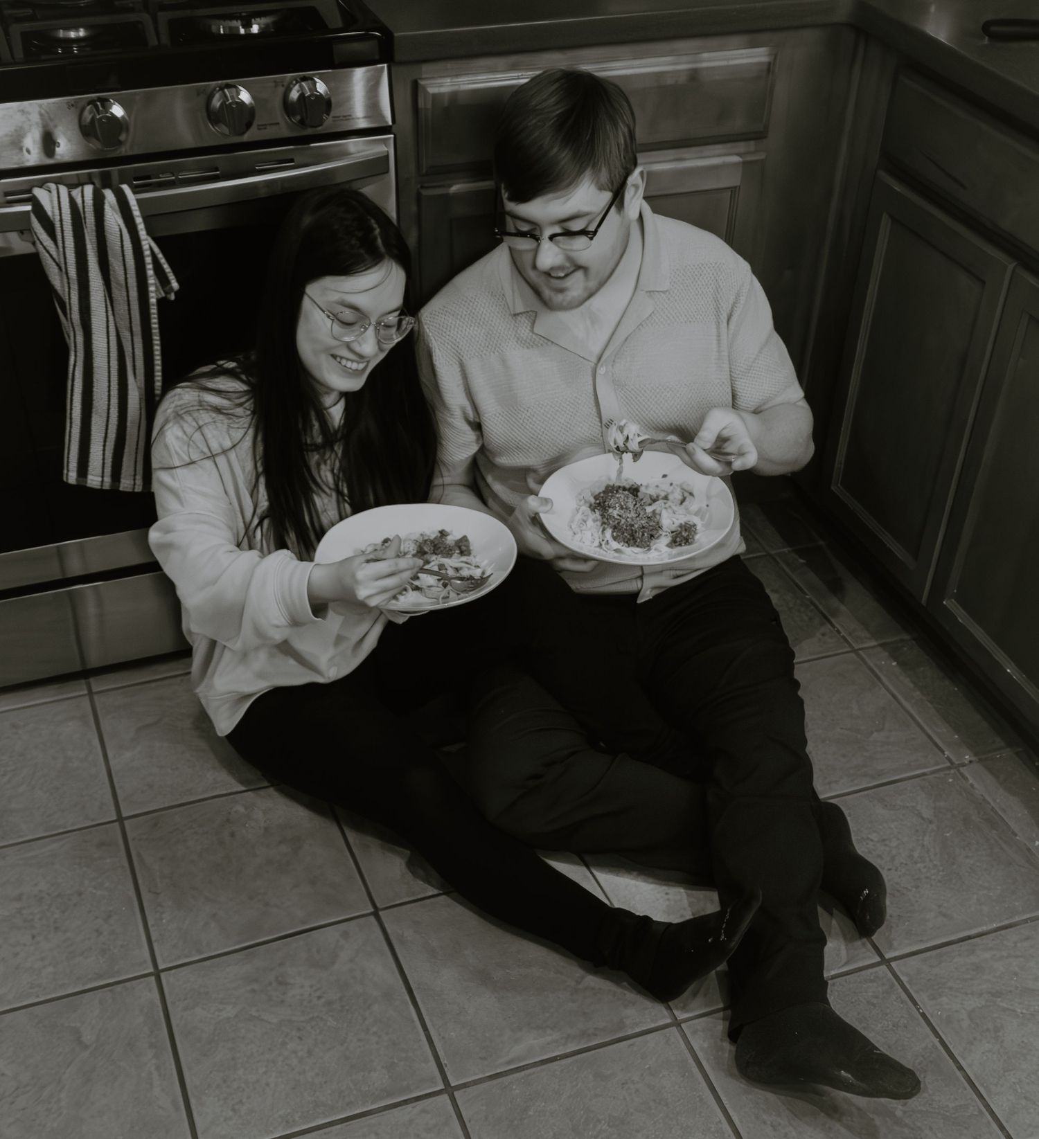 A couple sitting on their kitchen floor enjoying a homemade meal together.