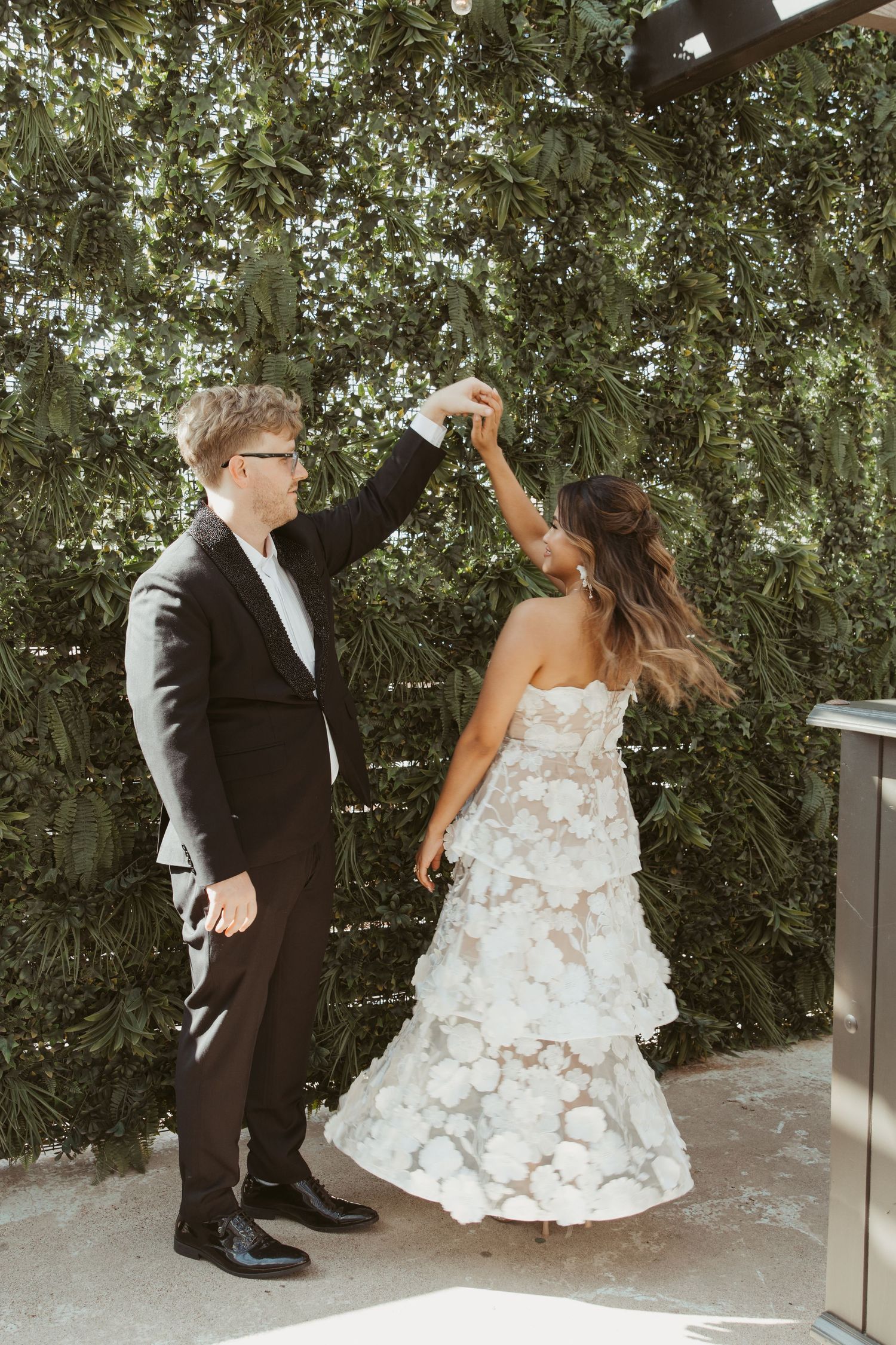 A playful wedding dance moment captured outdoors with greenery in the background.