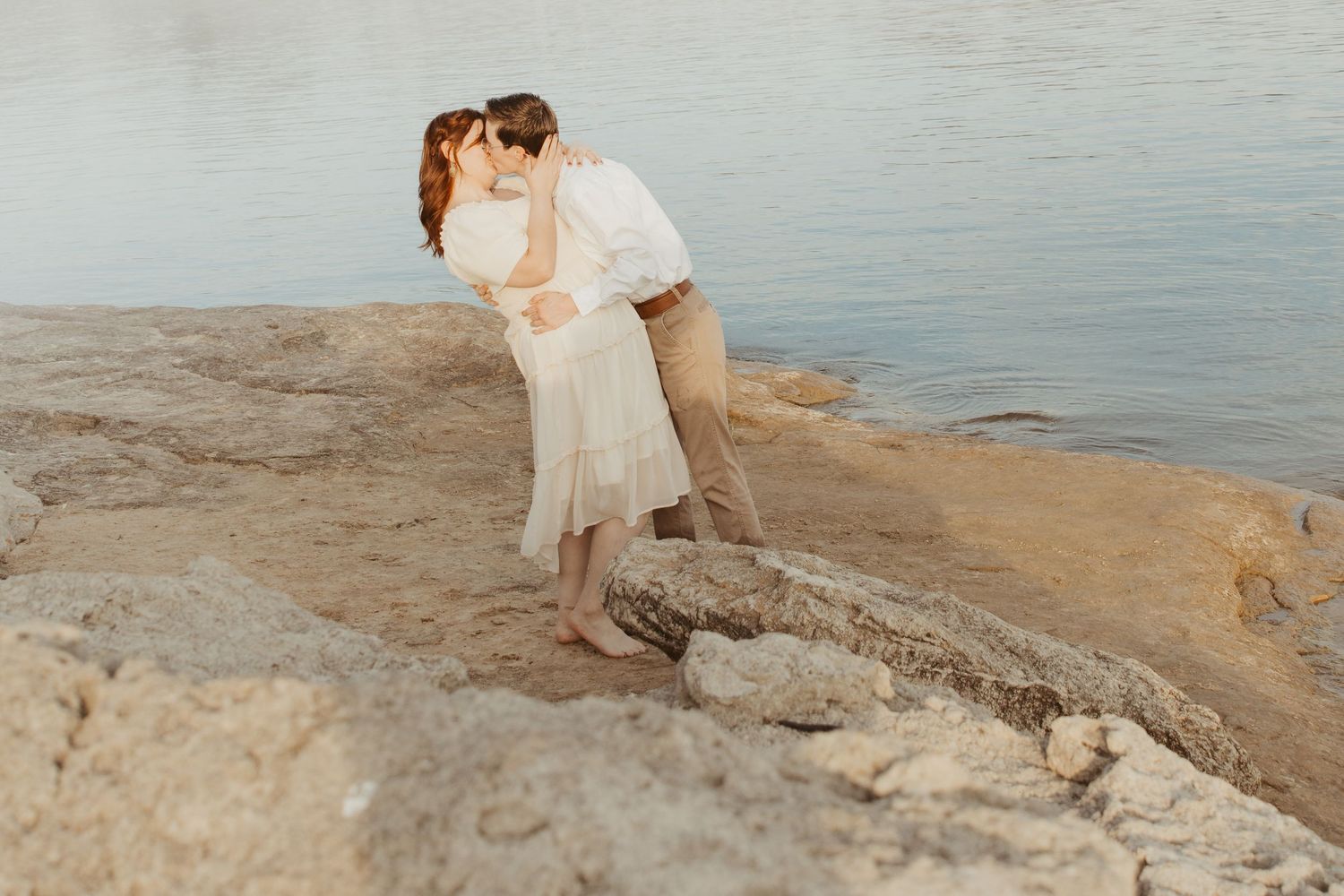 Two people dance together on a scenic coastal outcrop by the water.