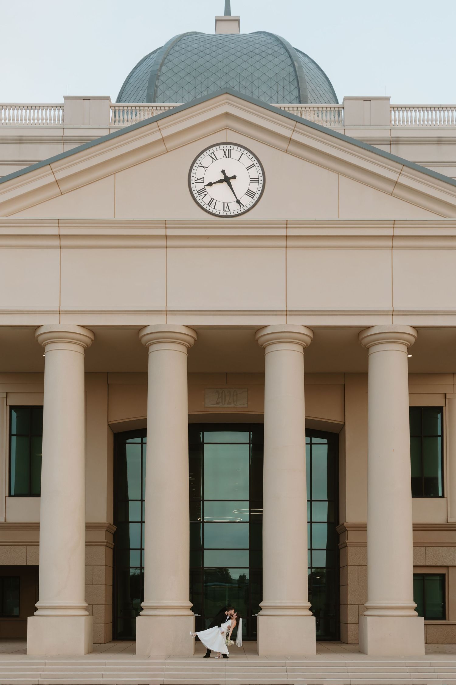 Wedding couple poses between grand white columns of a classical building with a domed roof. Wedding Photographer Fort Worth