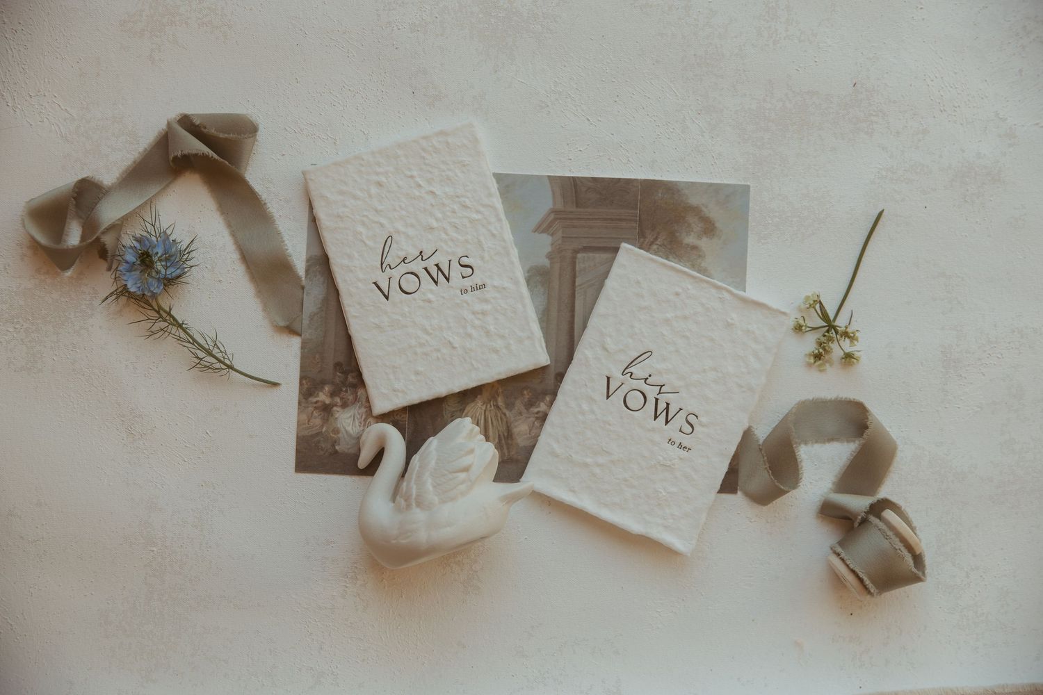 Elegant wedding vow books with floral accents, silk ribbon, and a swan figurine on a neutral background.