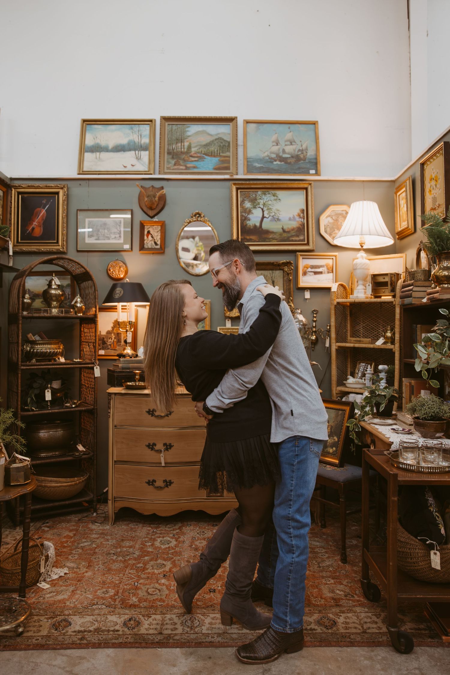 Couple exploring an antique store filled with vintage furniture, lamps, and framed artwork on display.