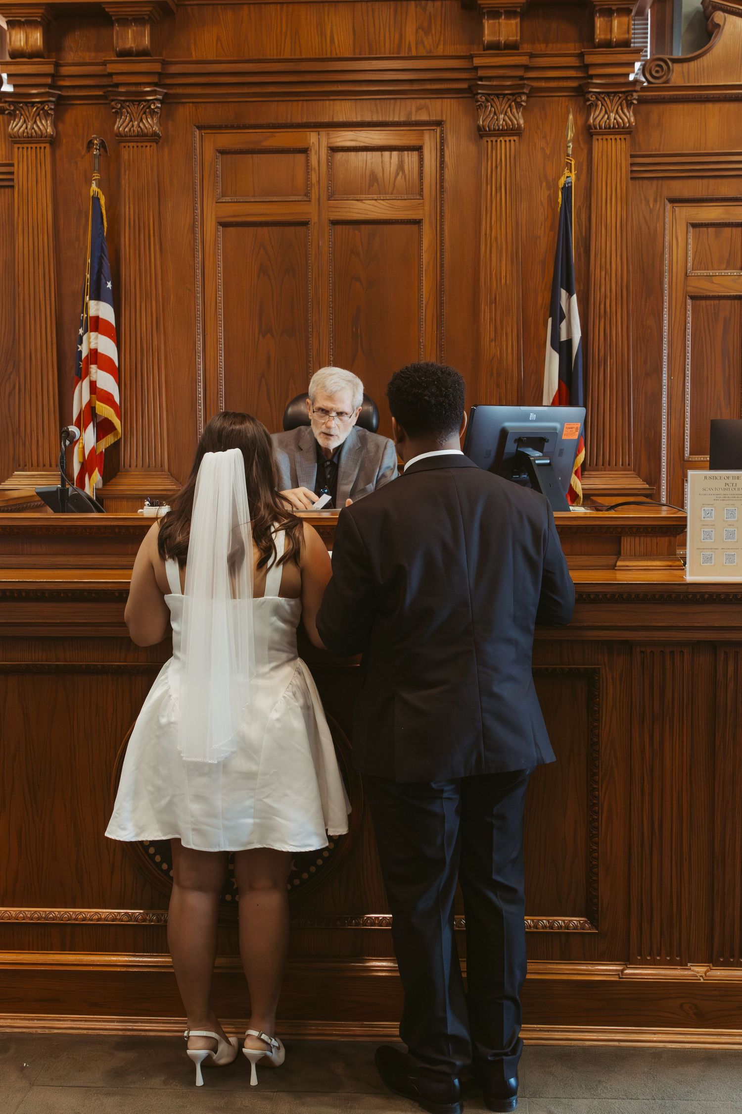A wedding ceremony takes place in a wood-paneled courtroom with American flags. Wedding Photographer DFW