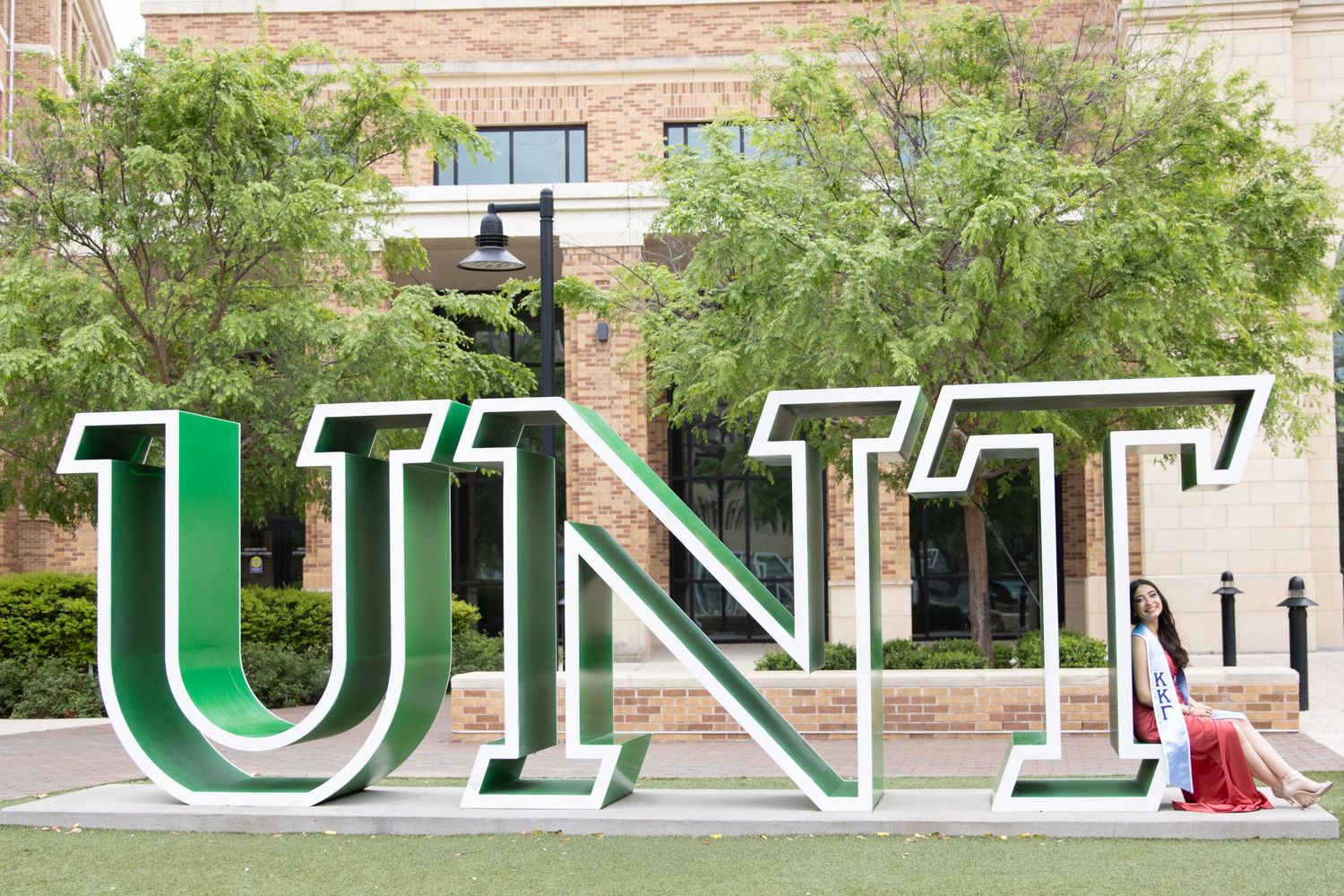 Large green UNT letters displayed on campus grounds with trees and buildings in the background.