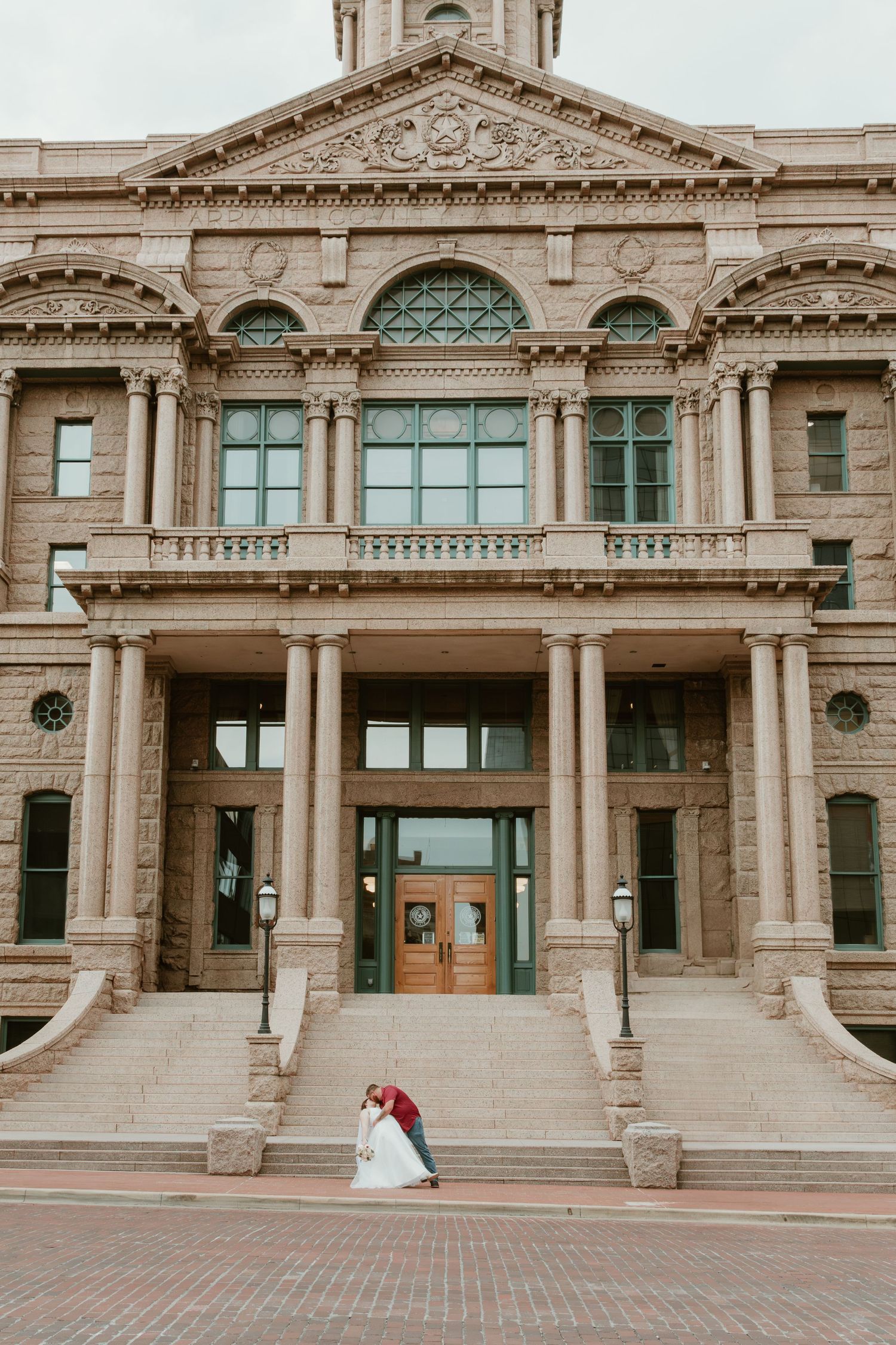 A grand historic courthouse with ornate architecture serves as backdrop for a wedding photo.