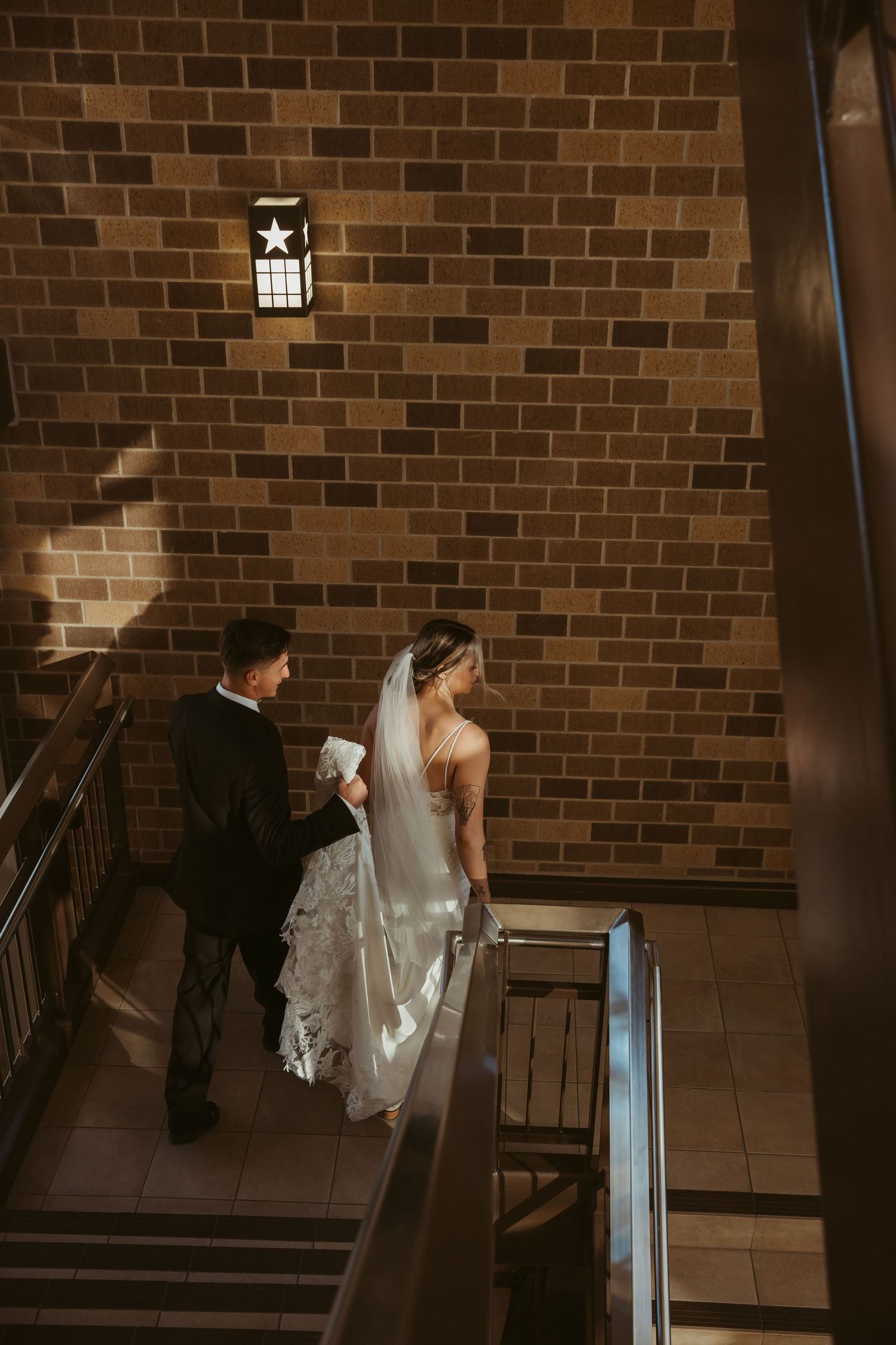 Bride and groom ascending a staircase together at a wedding venue with brick walls in dramatic lighting.