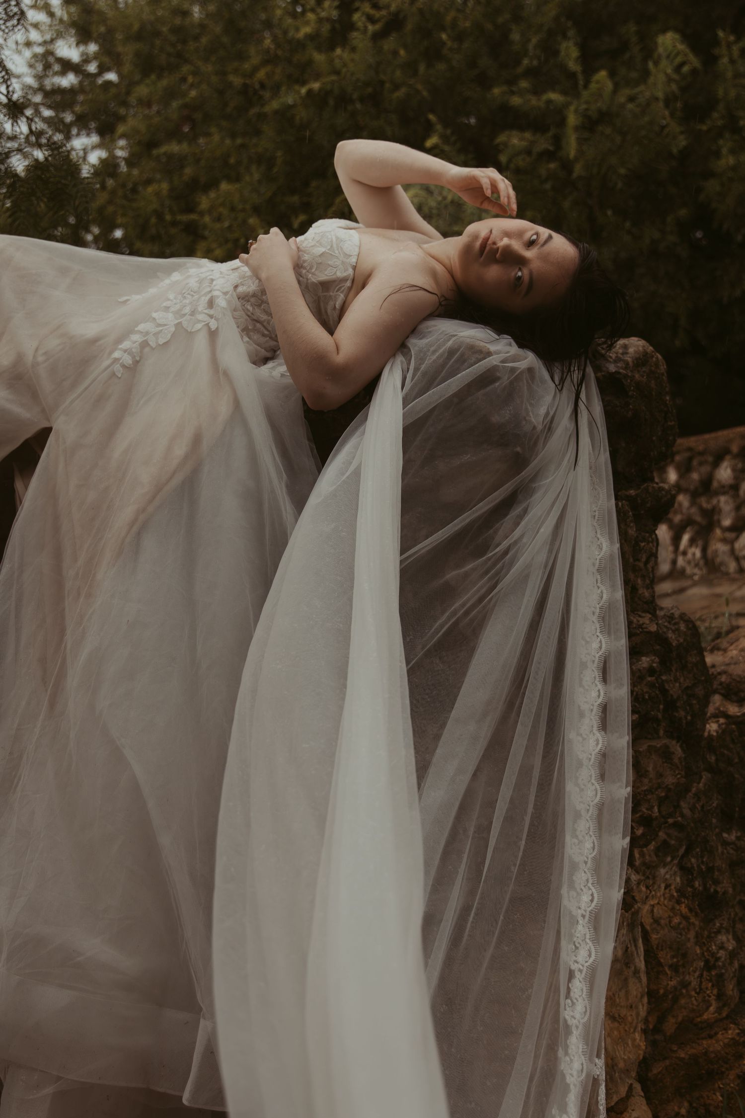 Artistic bridal photos featuring dramatic poses with flowing white veil and dress in natural setting.