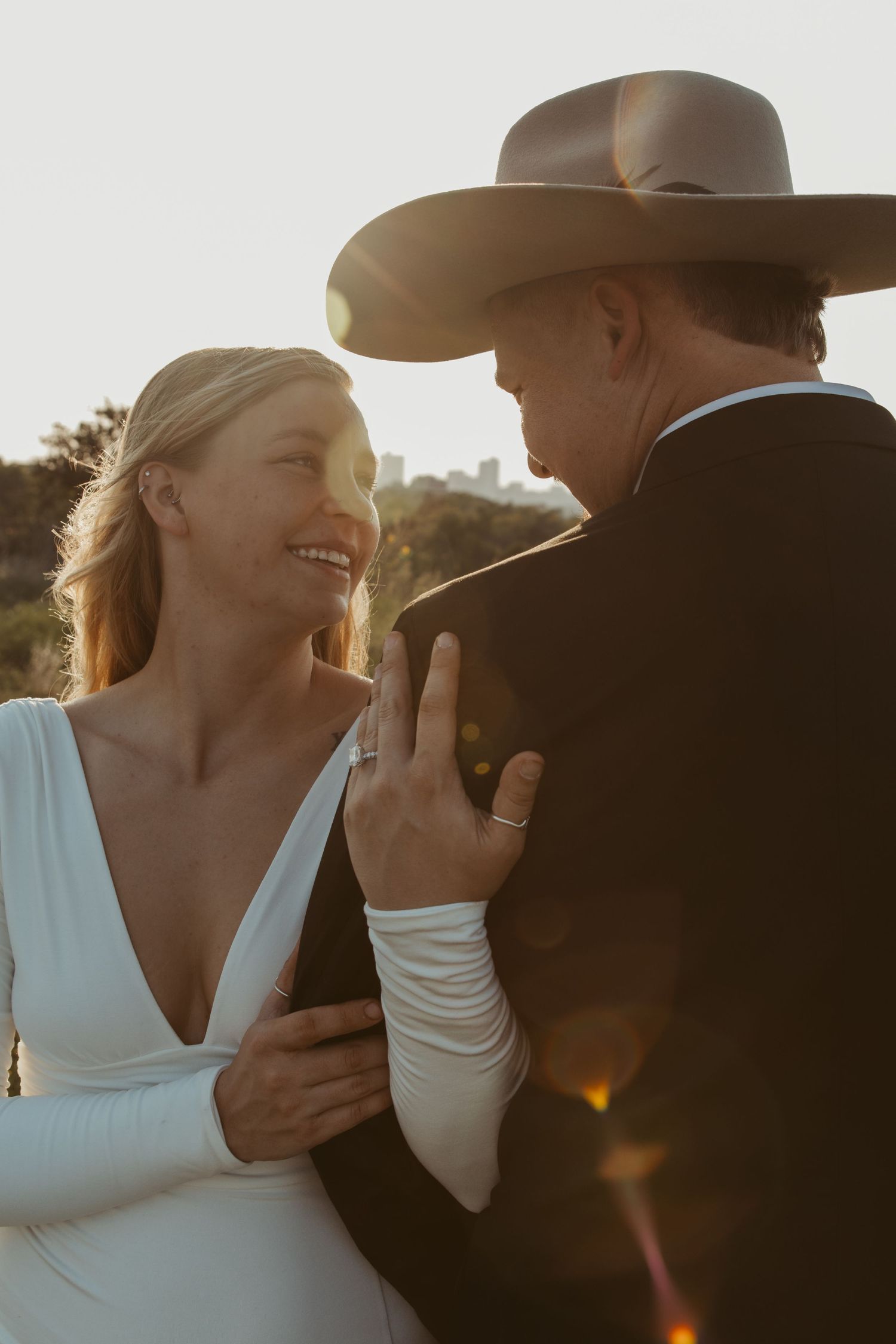 A romantic golden hour embrace between a couple wearing western attire in an outdoor setting.