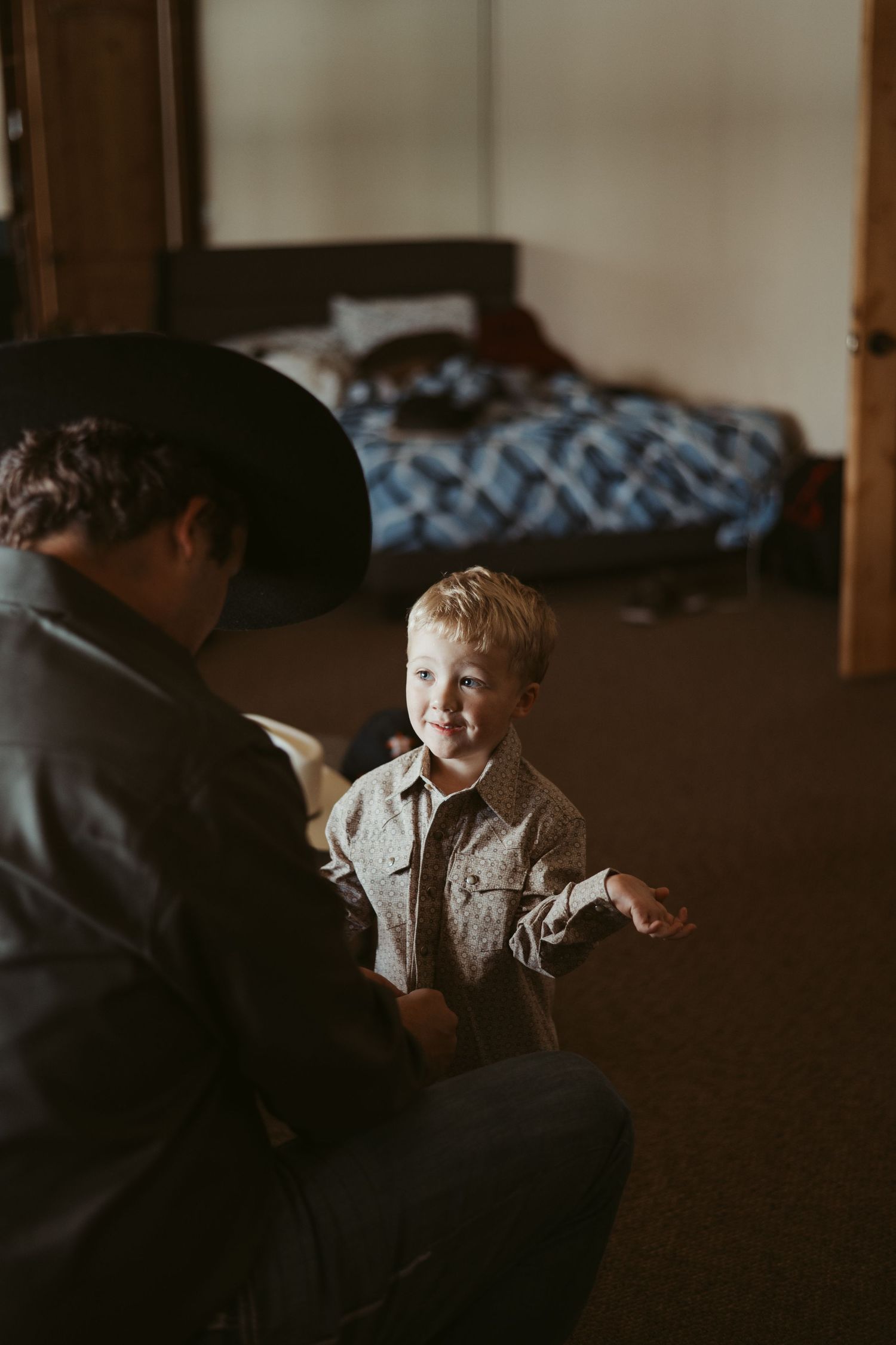 A young boy sits in dim lighting with a contemplative expression while wearing a light colored shirt. Wedding photographer DFW