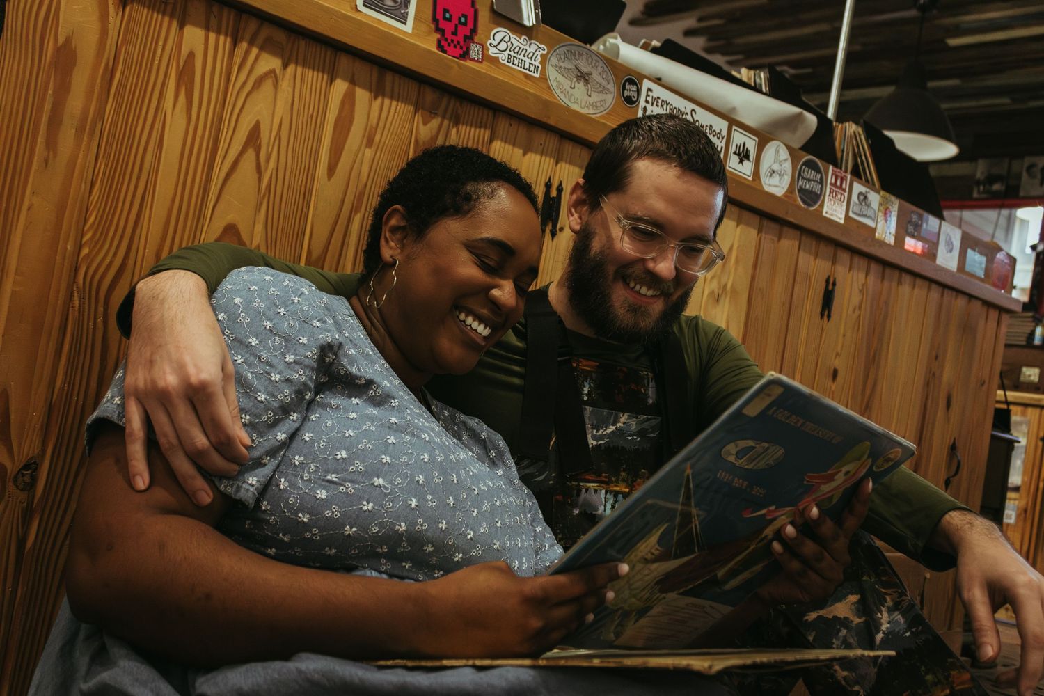 Two friends share a laugh while looking at a book or album together in a wood-paneled room.