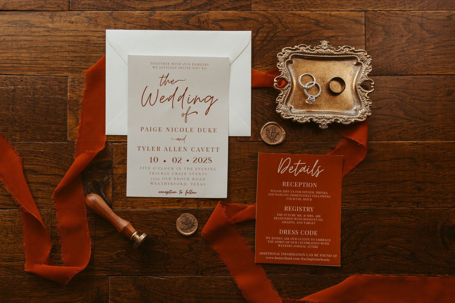 Wedding invitations and red ribbon details arranged on a dark wooden surface in warm, moody lighting. Wedding Photographer DFW