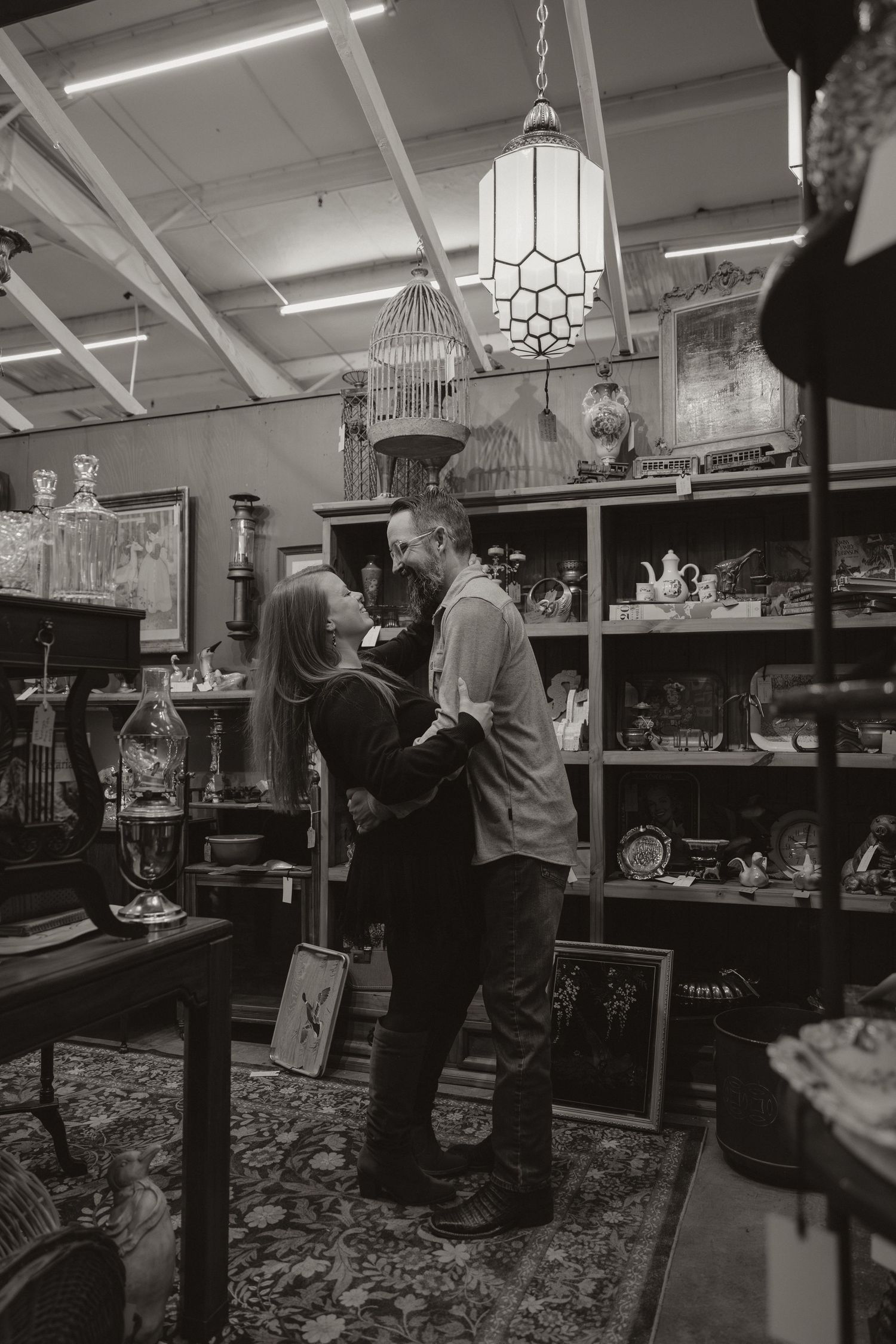 A couple shares an intimate moment in a vintage antique store filled with shelves of collectibles and an art deco pendant light.