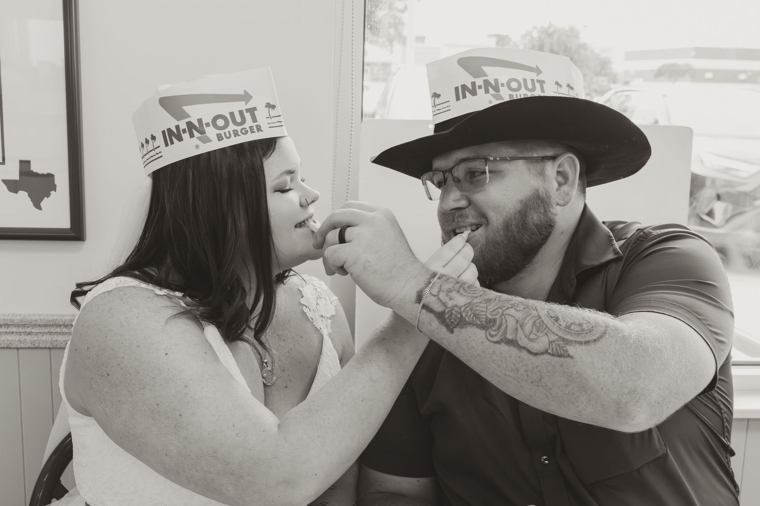 Black and white photo of a couple playfully feeding each other at an In-N-Out restaurant.