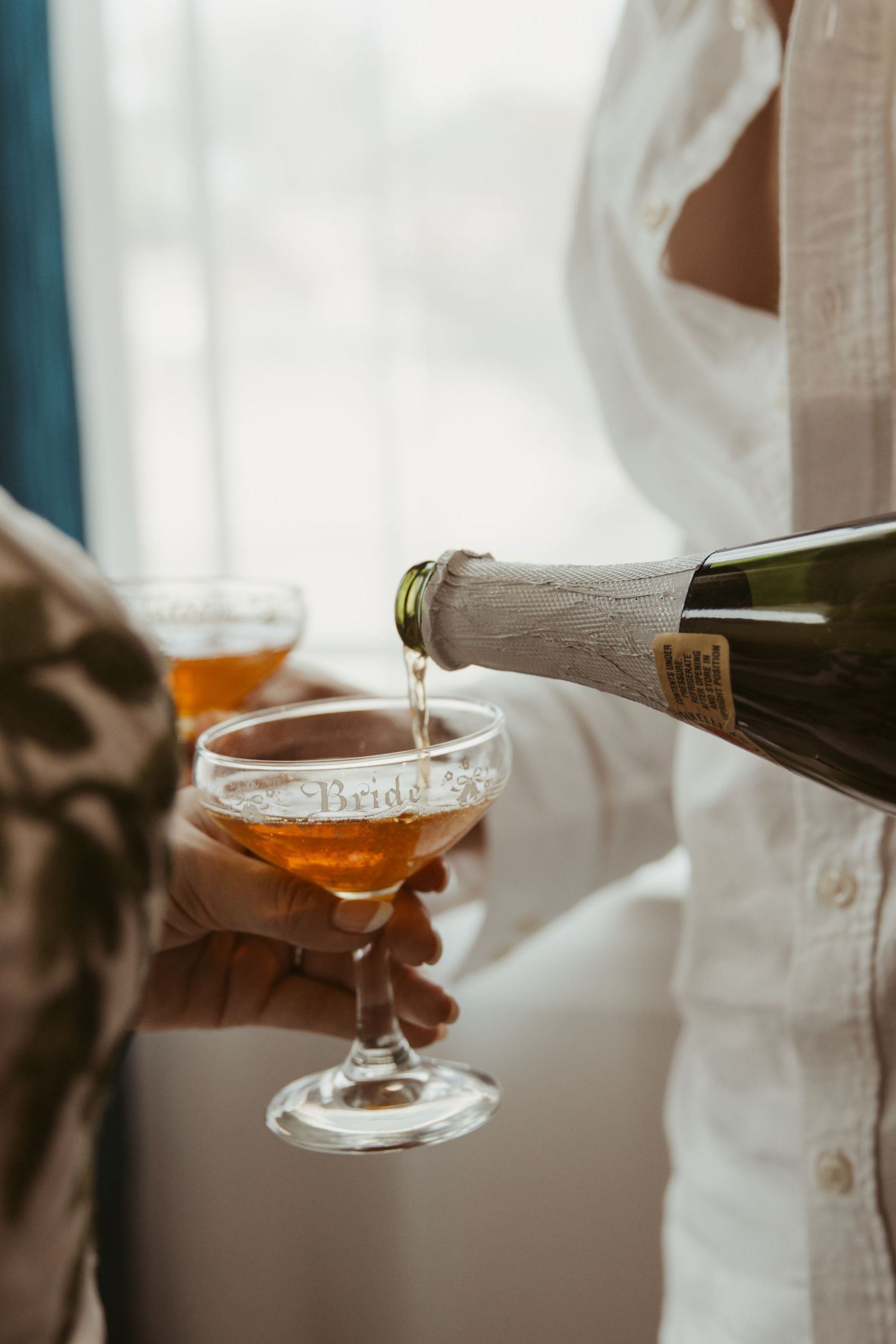 Hands pouring champagne into elegant coupe glasses during a celebration or event.