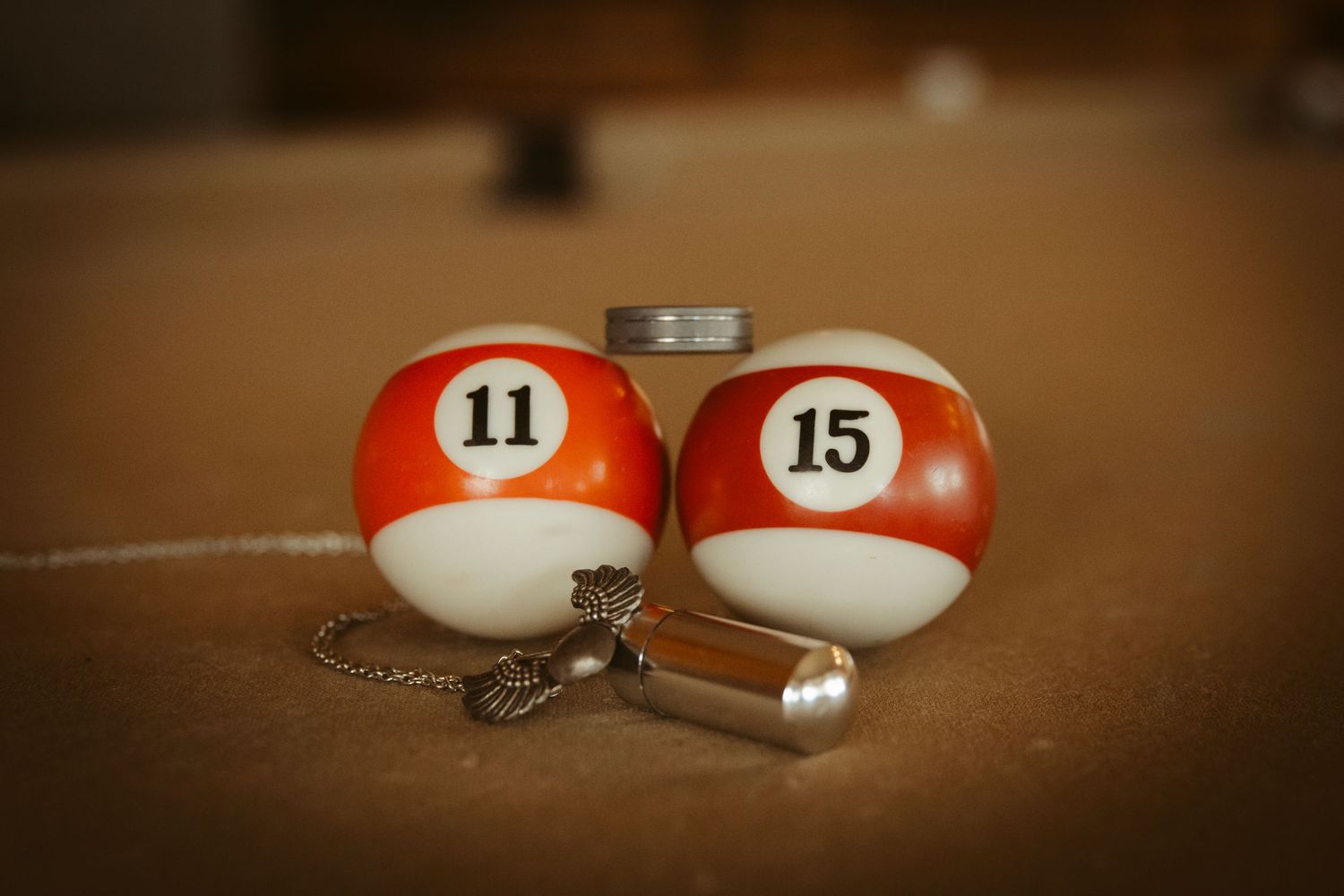 Two pool ball cue ball markers with numbers 11 and 15 attached to keychains on a brown surface. Wedding photographer DFW