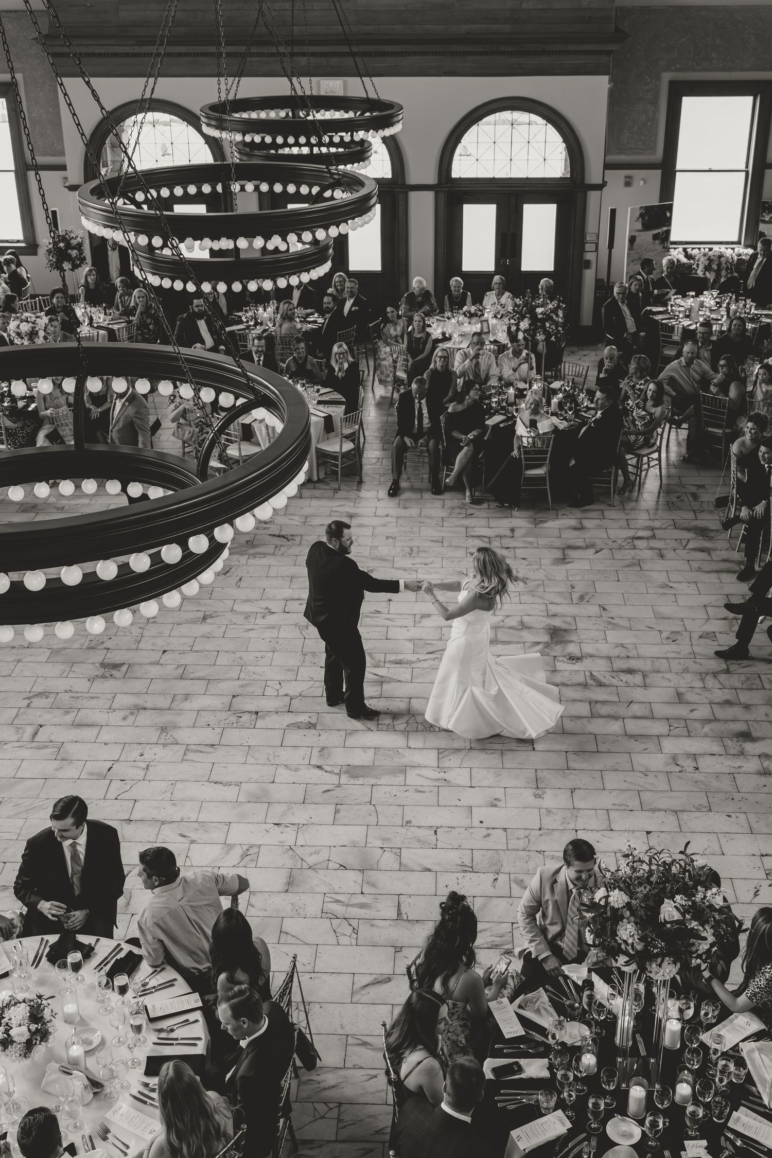 Black and white time-lapse sequence shows a couple dancing beneath an ornate chandelier at a formal ballroom event.