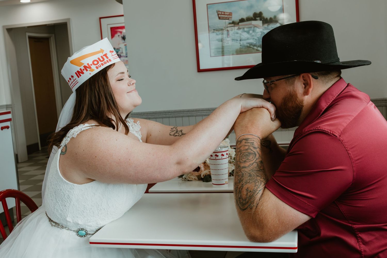 Playful couple wearing In-N-Out paper hats share a fun moment at a restaurant booth.