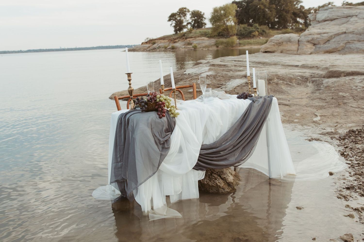 Elegant table setting on beach with flowing fabric and floral arrangements at sunset.