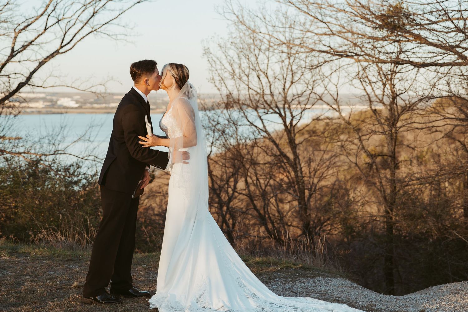 Newlywed couple shares romantic moments during sunset photoshoot in desert landscape with bare winter trees.