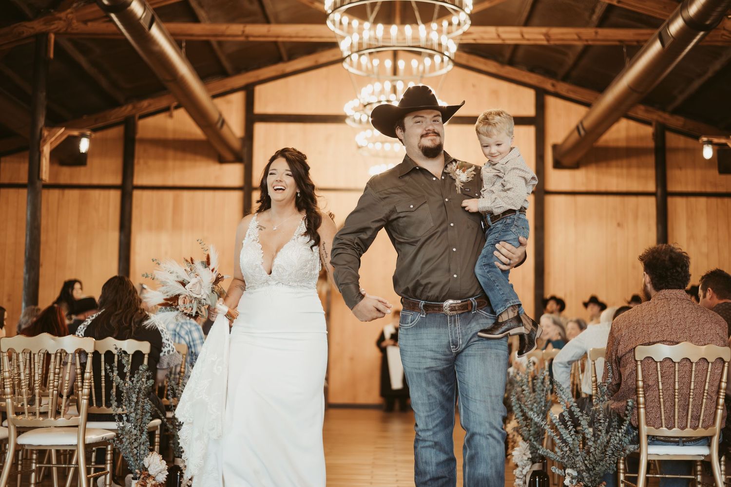 A couple celebrates during their rustic barn wedding reception with wooden beams and chandelier lighting. Wedding photographer DFW