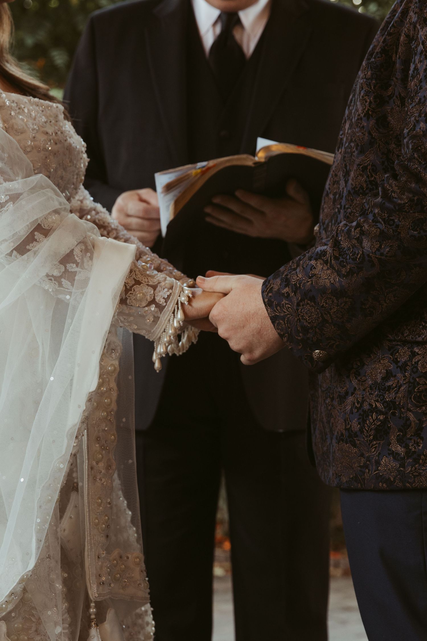 Close-up shot of a wedding ceremony showing couple's hands and an officiant holding a book during the vows.
