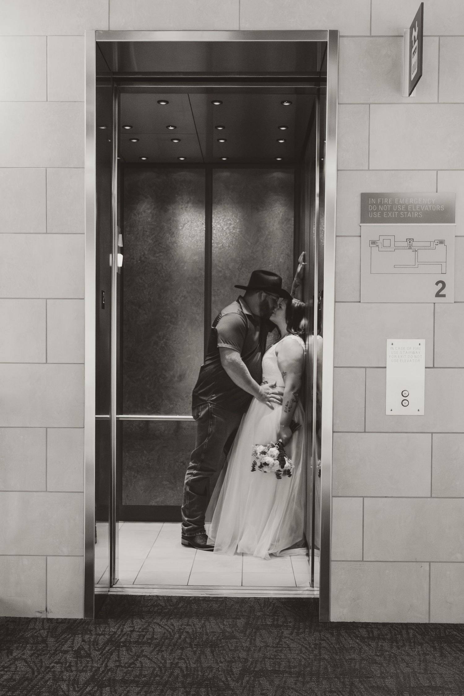 Black and white photo of wedding couple entering elevator in modern building.