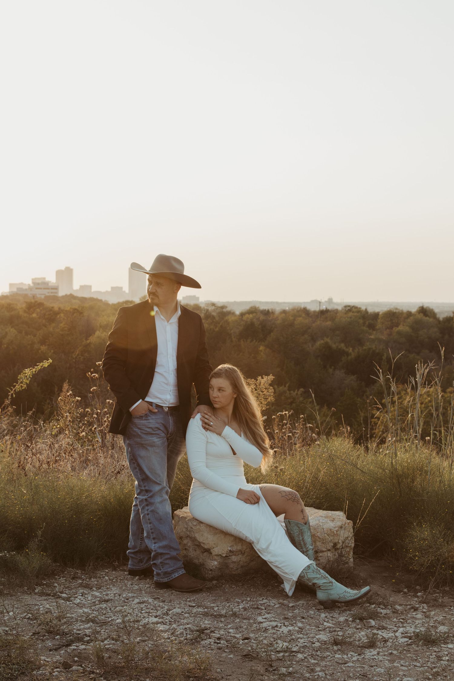 A couple sits together on a rocky overlook during golden hour in a romantic outdoor setting.