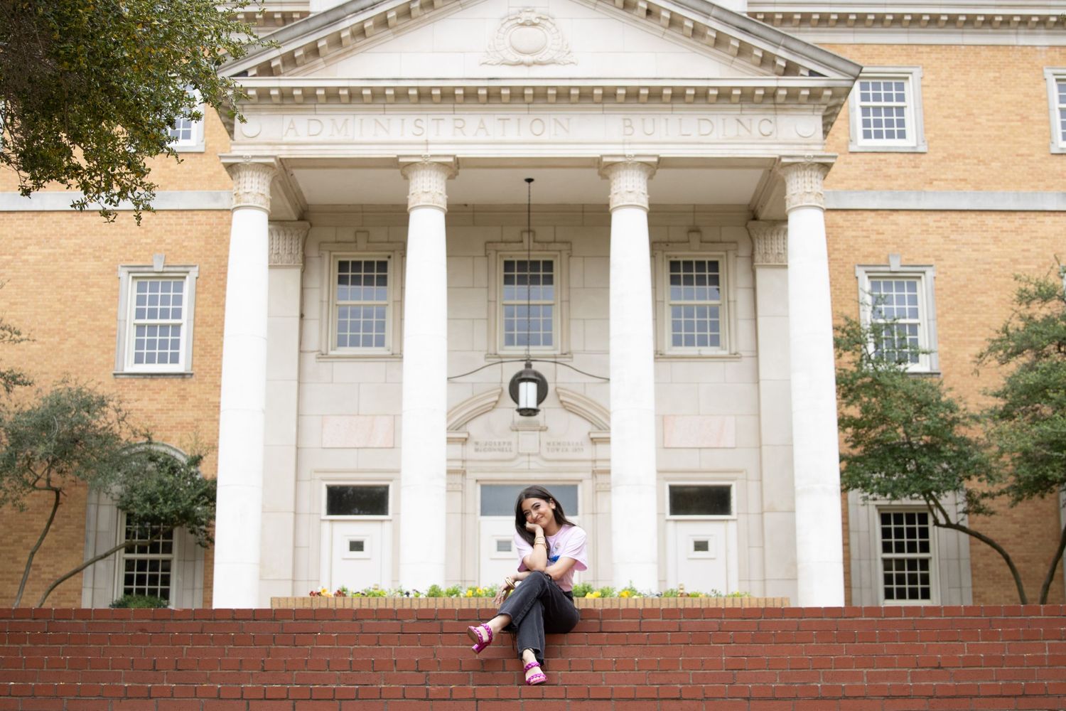 A couple sits on red brick steps in front of a grand white columned building entrance with Greek Revival architecture.