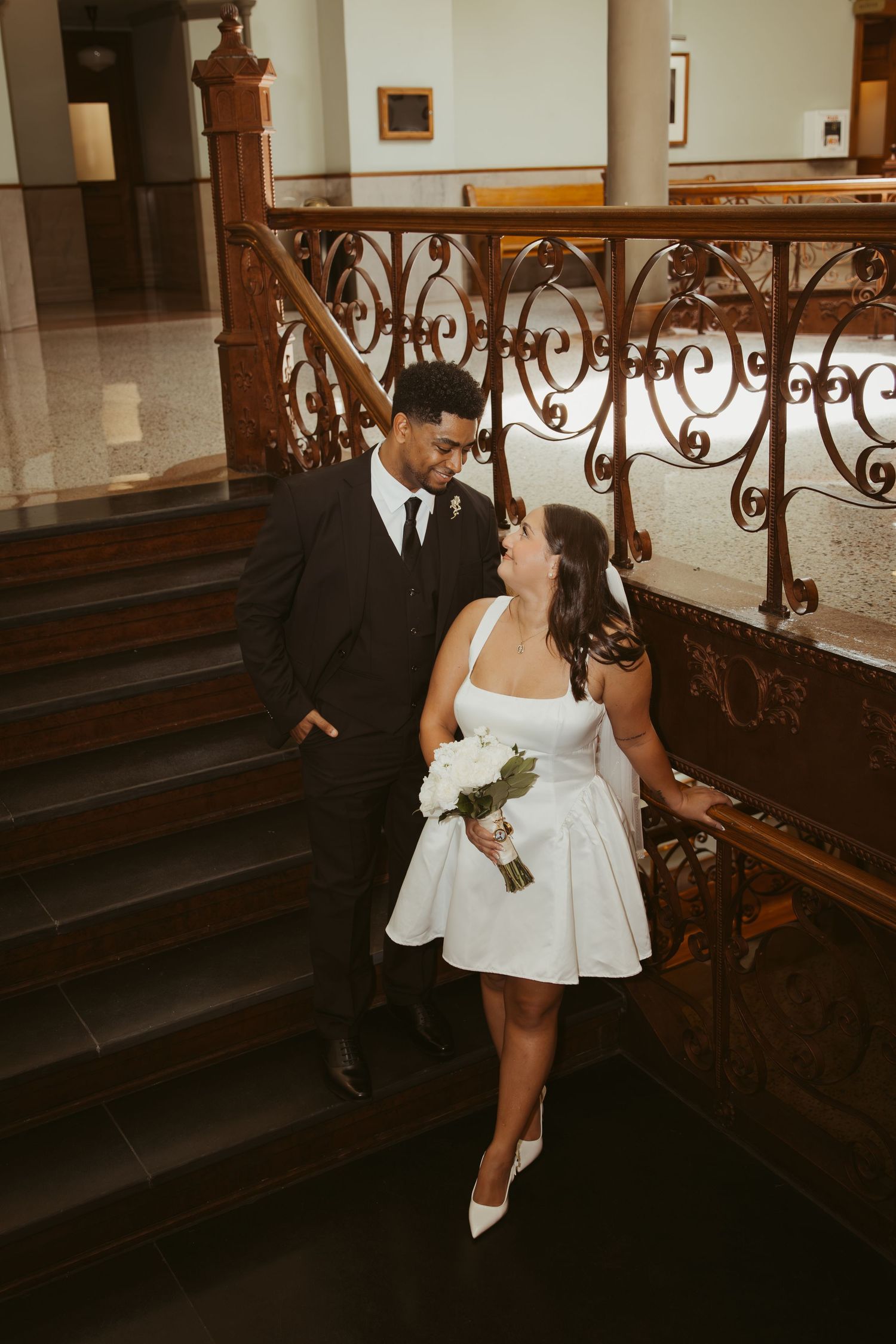 A couple in wedding attire poses near ornate iron railings and stairs. Wedding Photographer DFW