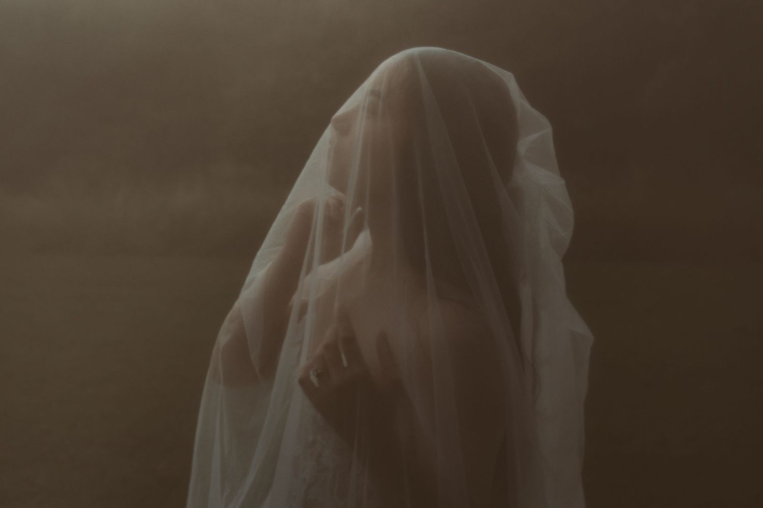 A ghostly figure draped in translucent white fabric stands against a dark moody background.