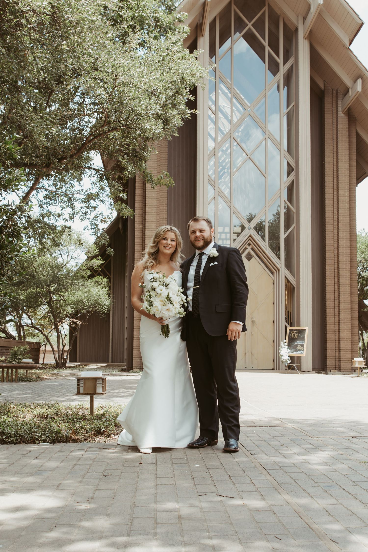 A wedding couple stands outside a modern church building with tall geometric windows and stone architecture.