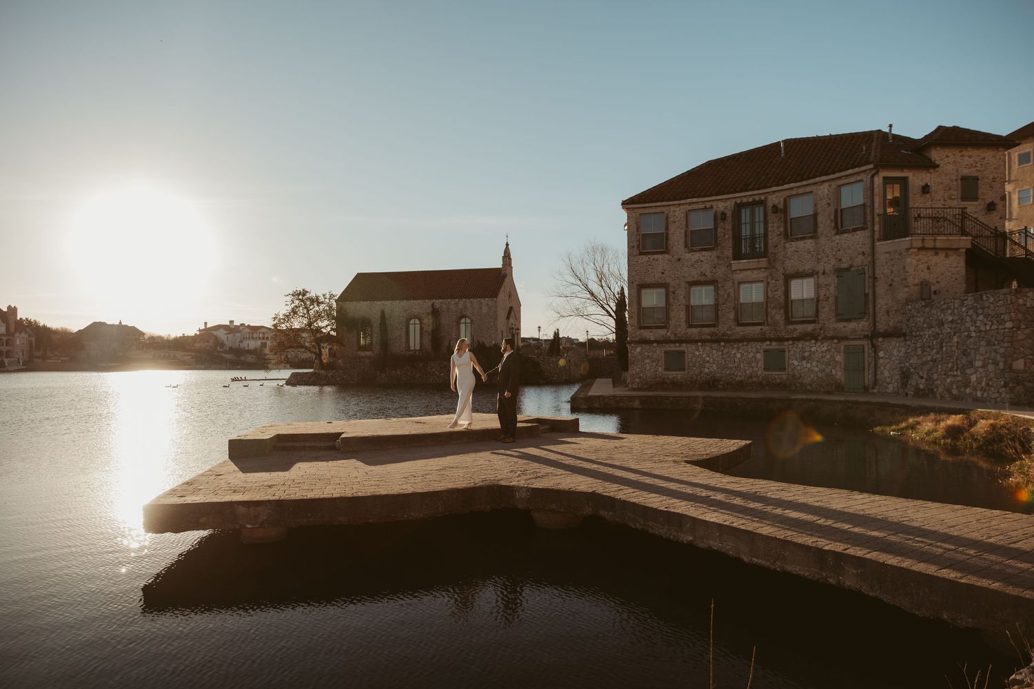 Coastal panorama at sunset showing a stone pier and buildings along a Mediterranean waterfront.