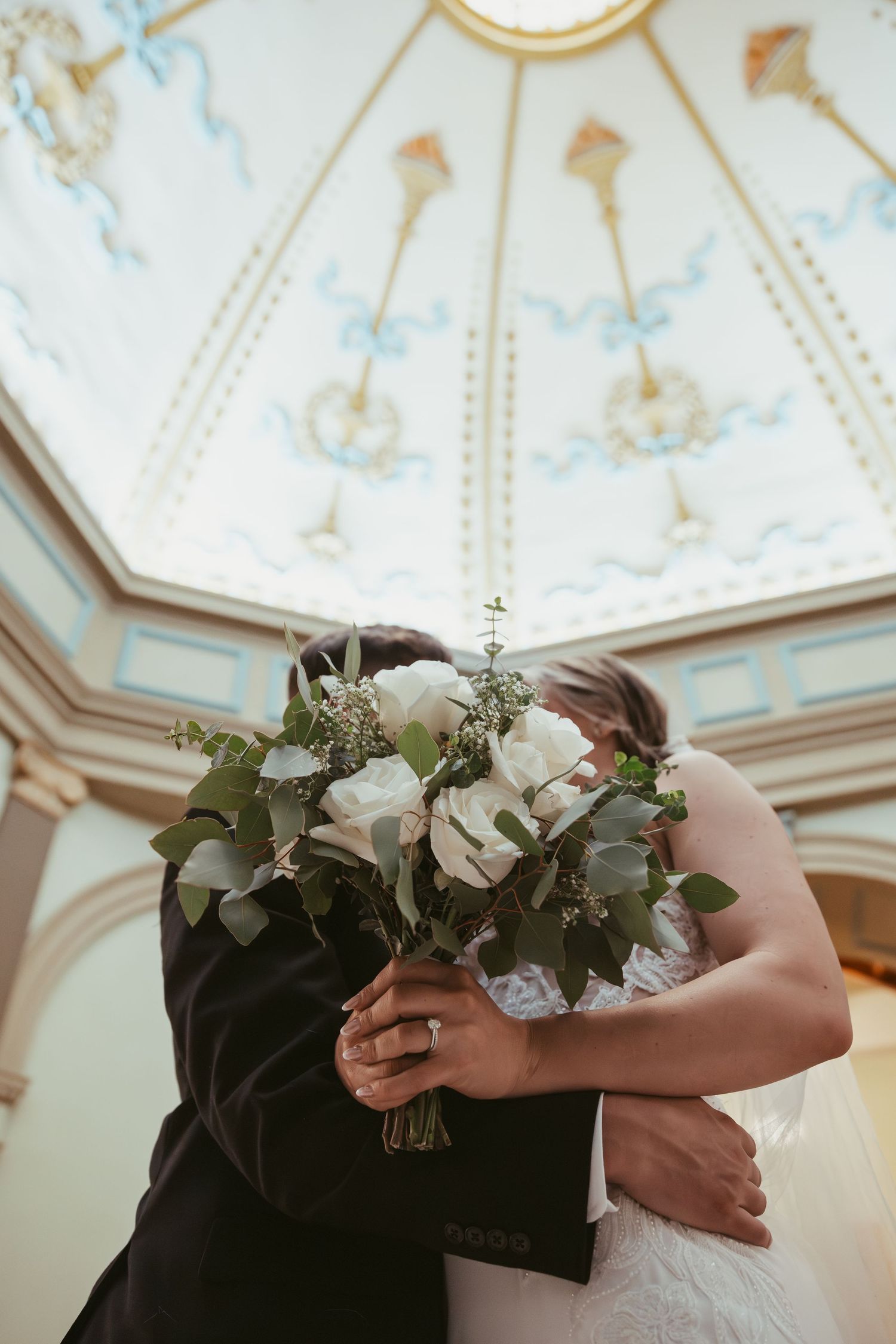 A romantic wedding scene with white floral bouquets and a decorative domed ceiling with light blue details.