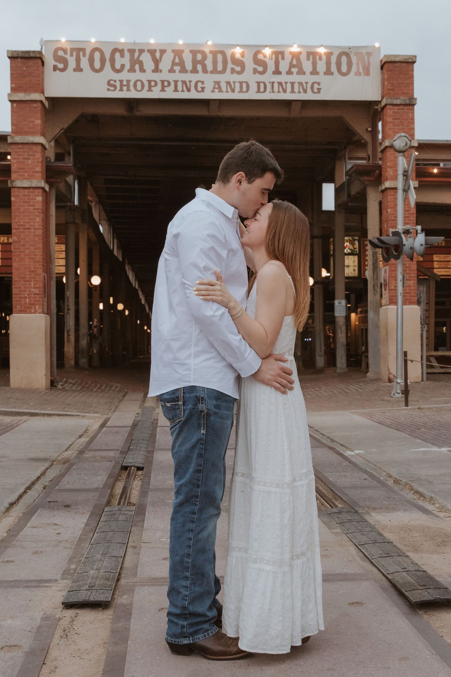 A romantic couple embraces under the Stockyards Station shopping and dining sign in Fort Worth, Texas.
