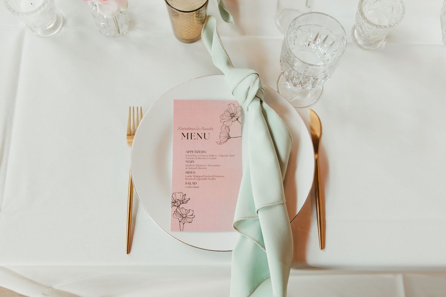 Elegant wedding table settings with mint green napkins, gold utensils, and pink menu cards.