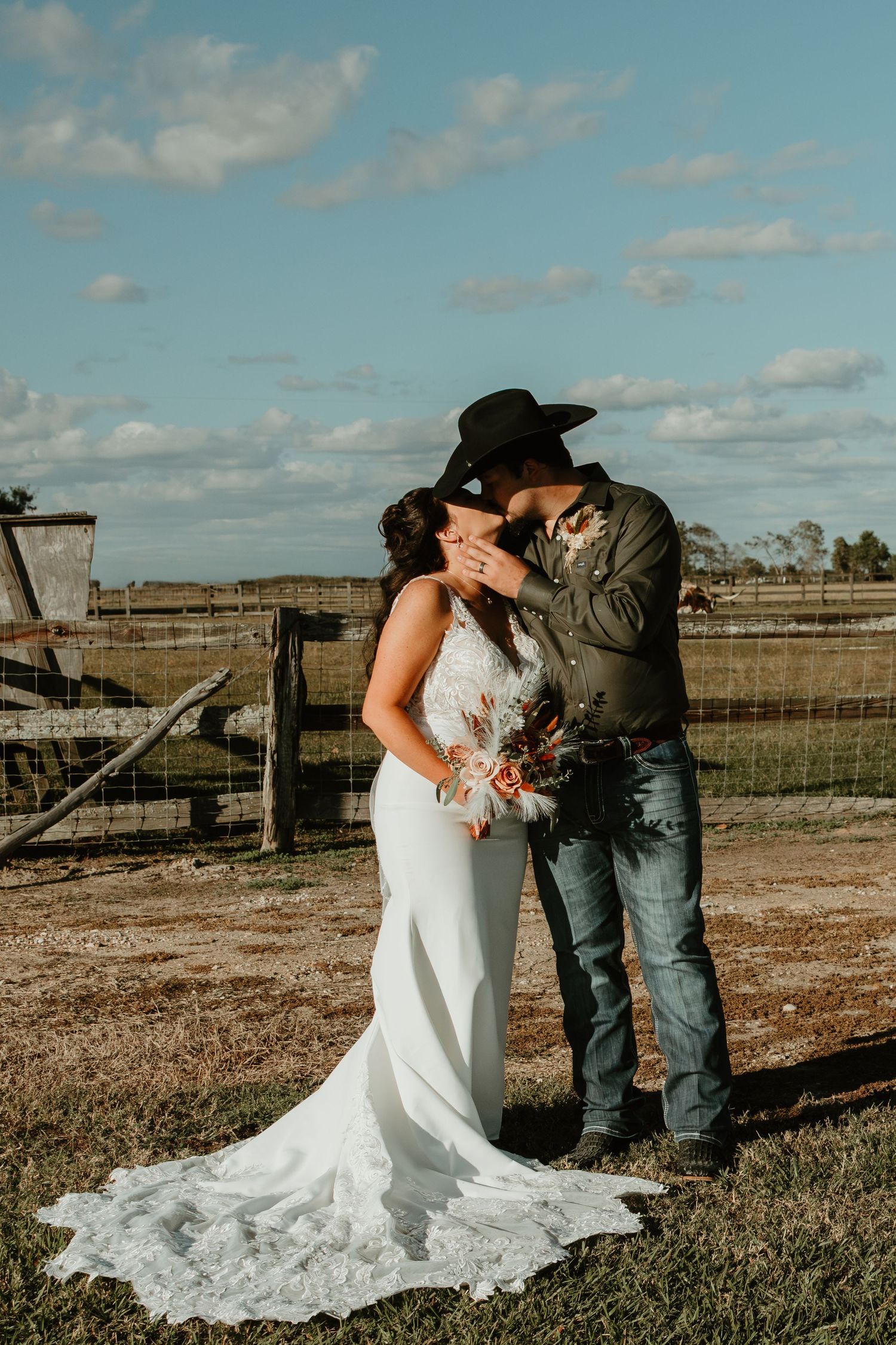 Wedding couple embracing in an outdoor field with wooden fencing and blue sky. Wedding photographer DFW