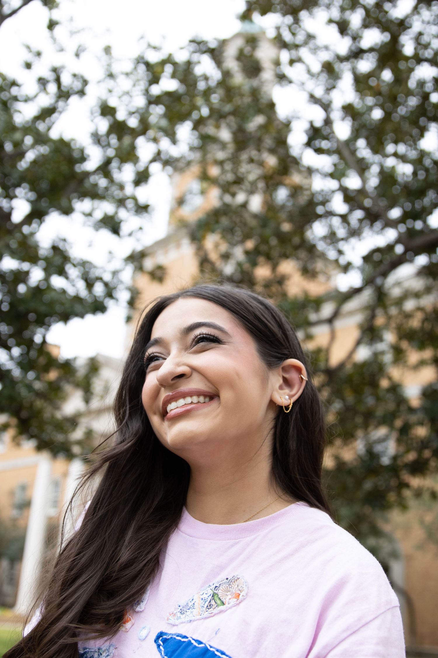 Joyful person wearing a pink graphic t-shirt smiling outdoors with trees in the background.