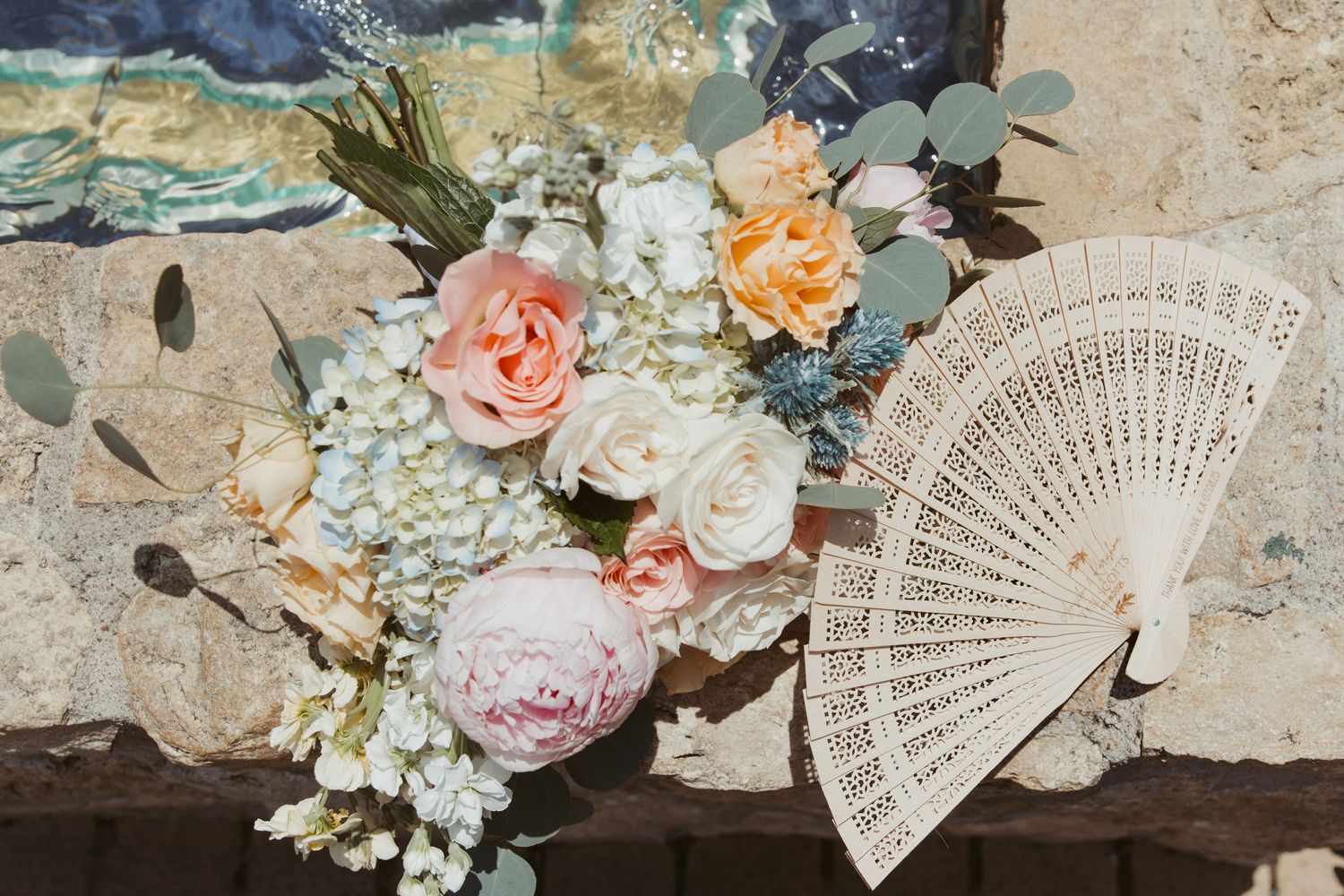 Delicate pastel floral arrangements with white lace fans displayed on rustic stone surfaces.
