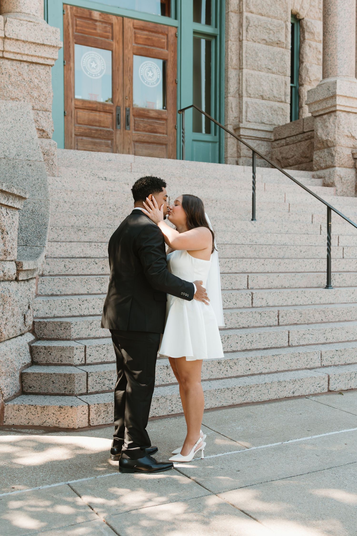 A couple shares a romantic moment on the steps of a stone building. Wedding Photographer DFW