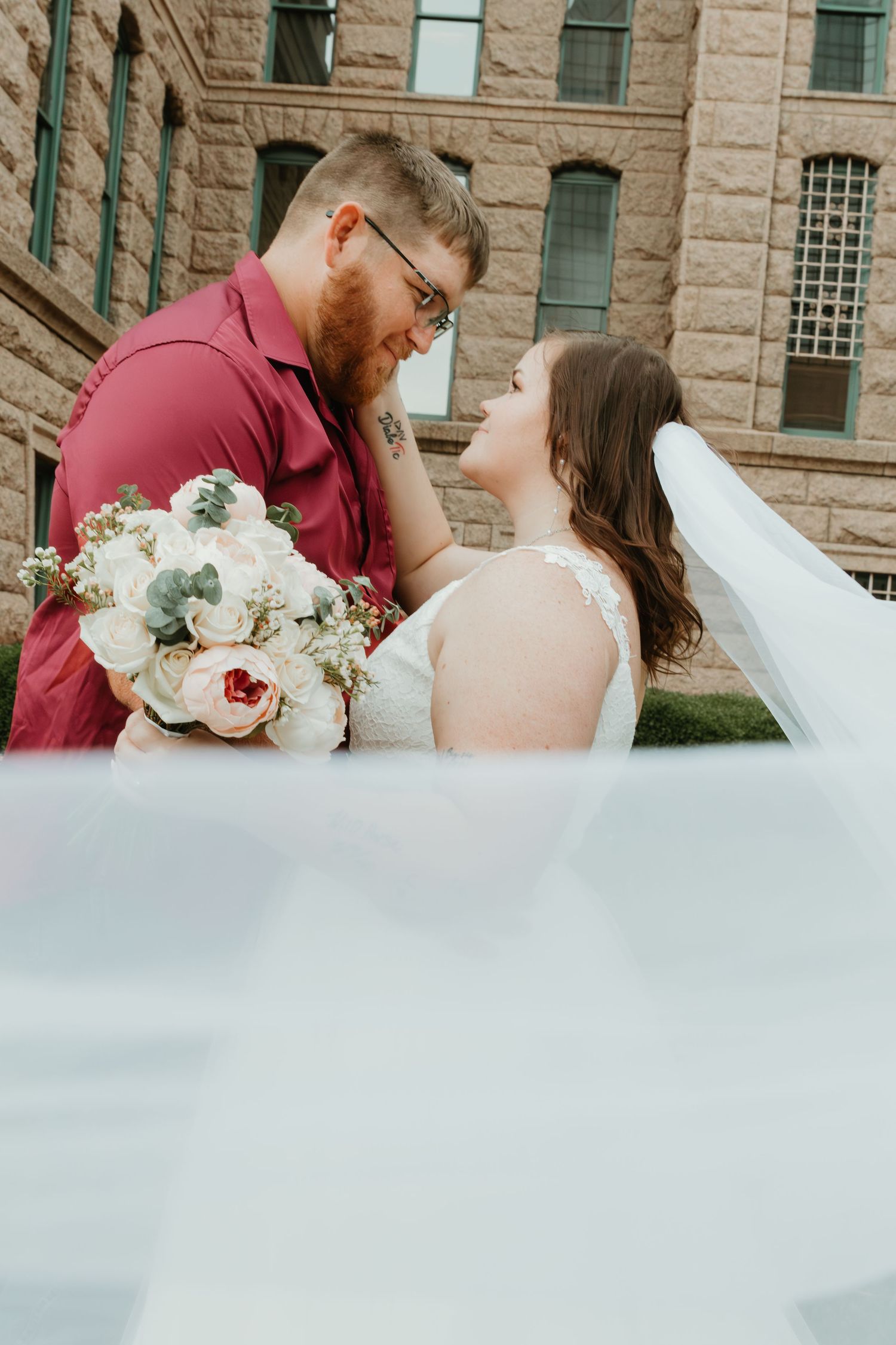A romantic wedding moment with a beautiful bridal bouquet featuring white and blush flowers against a stone building.